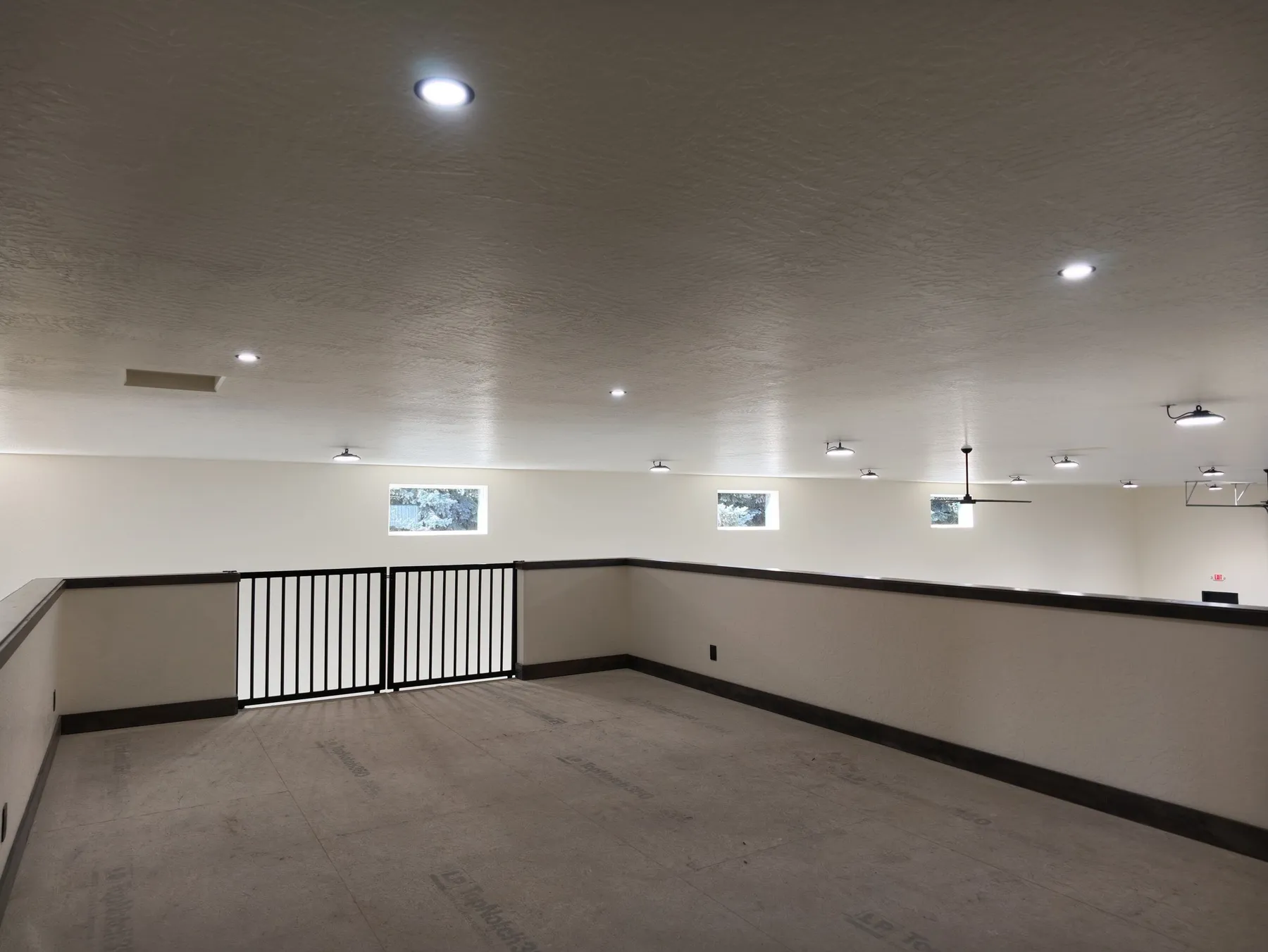 Mezzanine level overlooking the warehouse, with a concrete floor, small high windows and a black metal safety gate.
