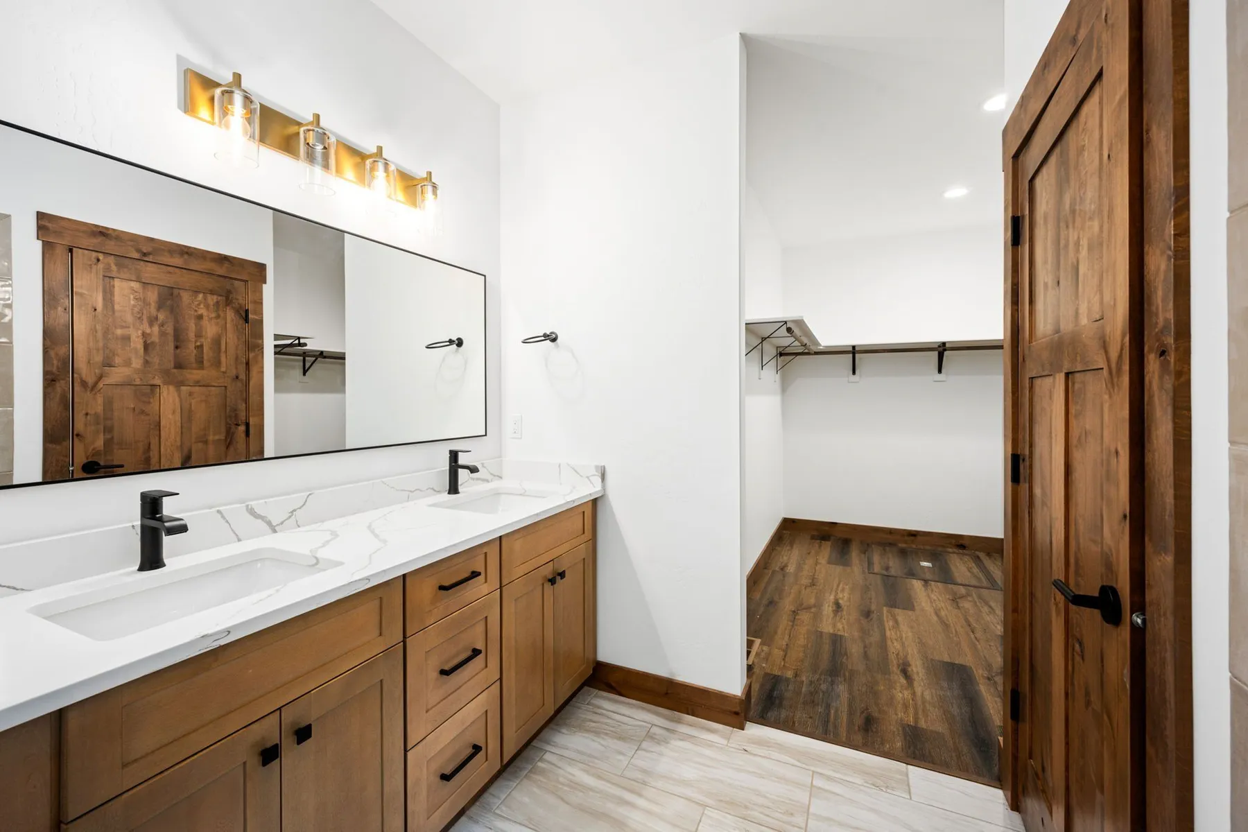 Bathroom with a double vanity facing a large mirror, with the walk-in closet beside it.