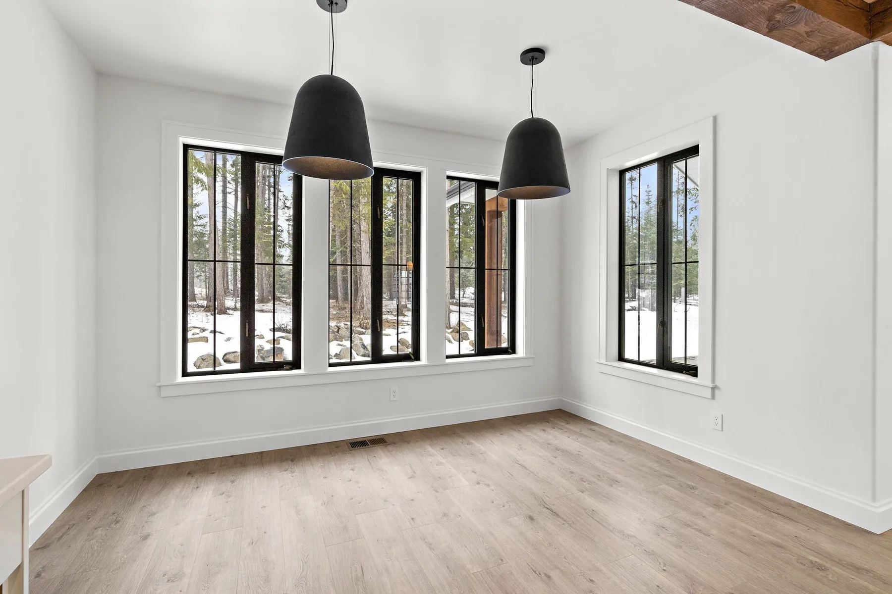 Dining area with two black dome pendants and tall black-framed windows looking onto a snowy wooded lot.