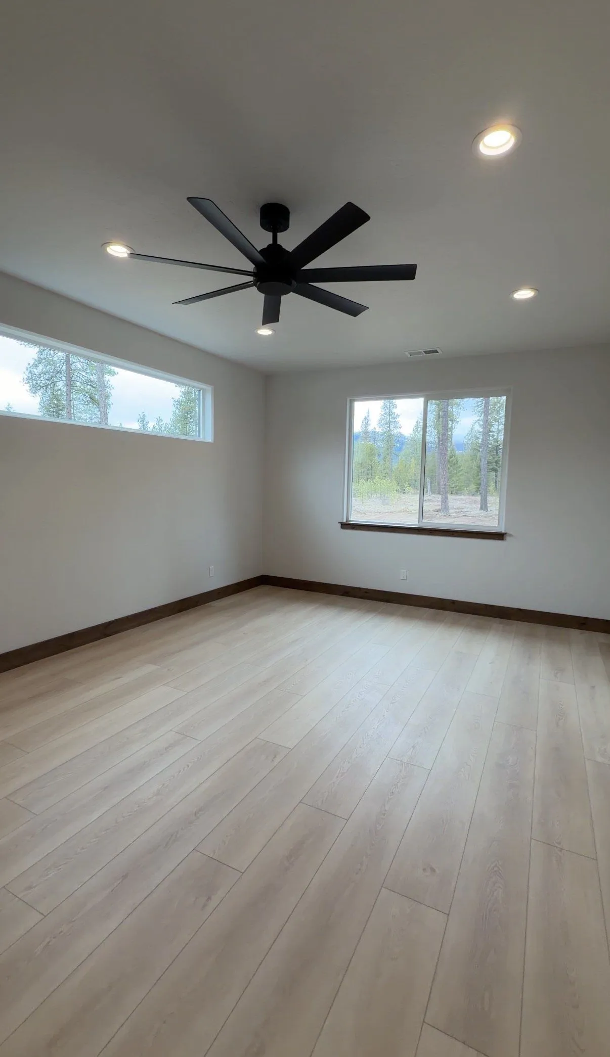 Bedroom with a large black ceiling fan, a clerestory window and a window looking out to the pines.