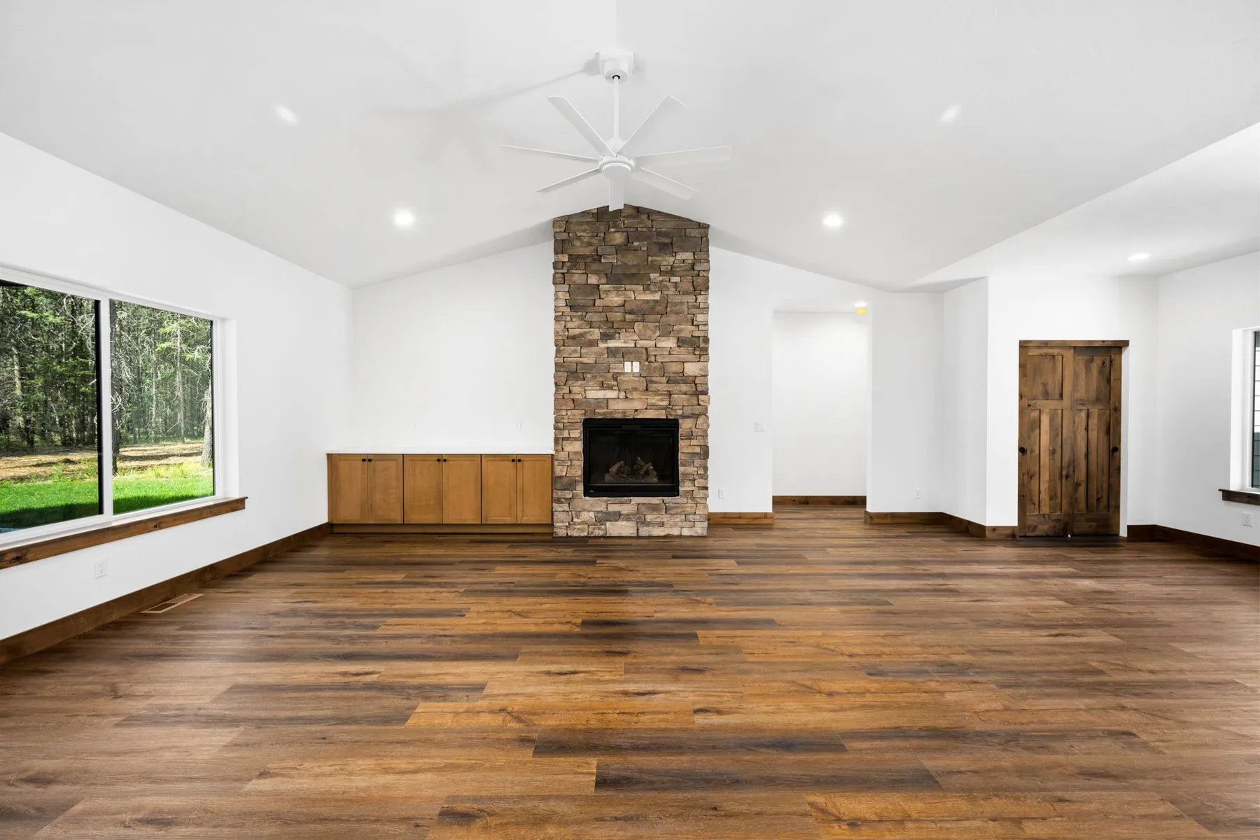 Vaulted great room with a stone fireplace, built-in cabinets and a large window to the forest.