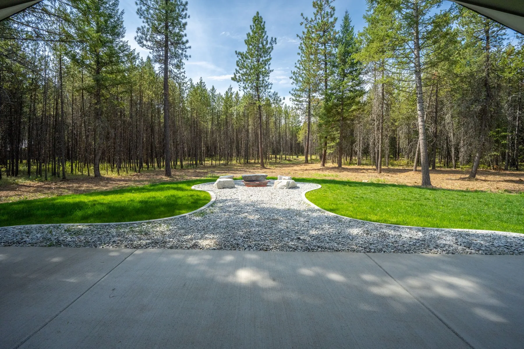 View from the covered patio across the lawn and a white-rock path to a fire pit at the edge of the pine forest.