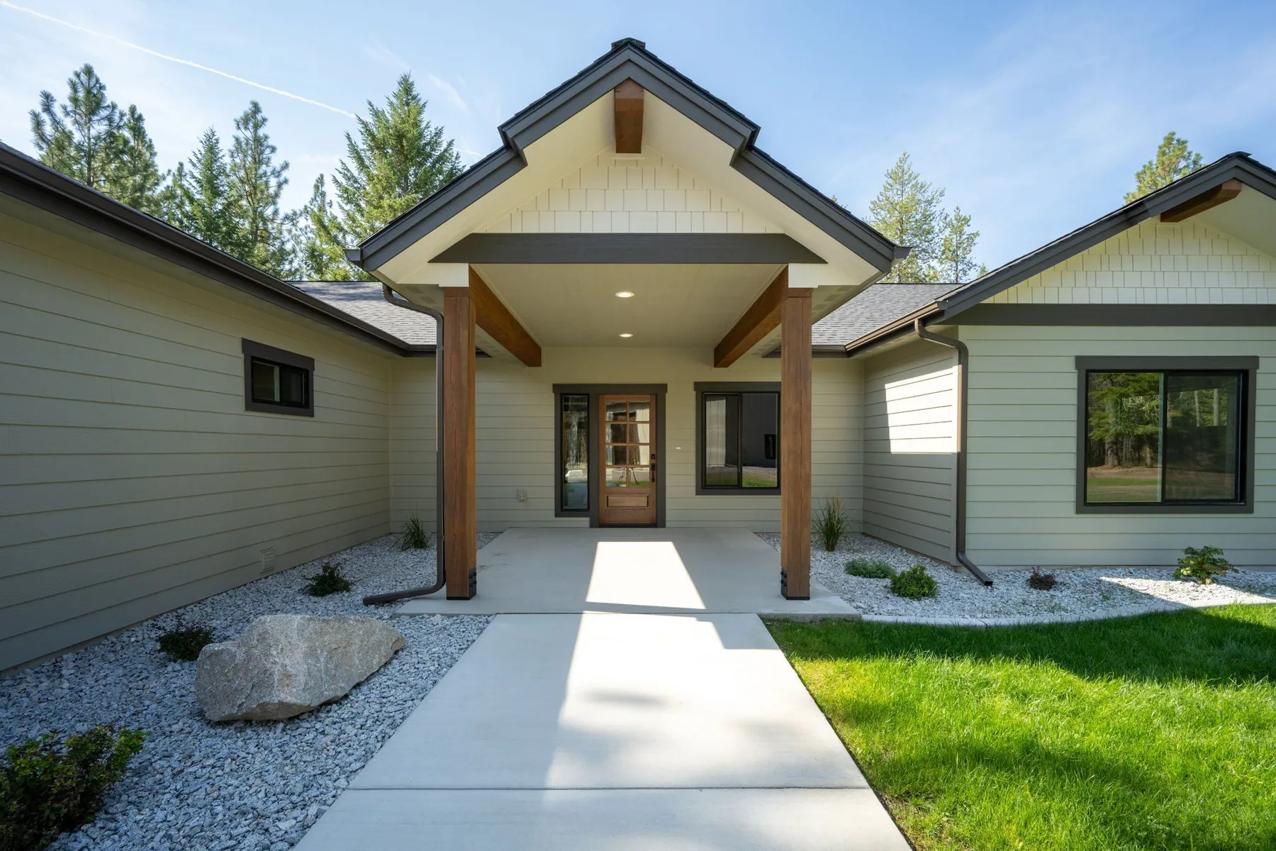 Covered front entry with a timber-framed gable, a wood door with glass panels and a concrete walk bordered by white rock.