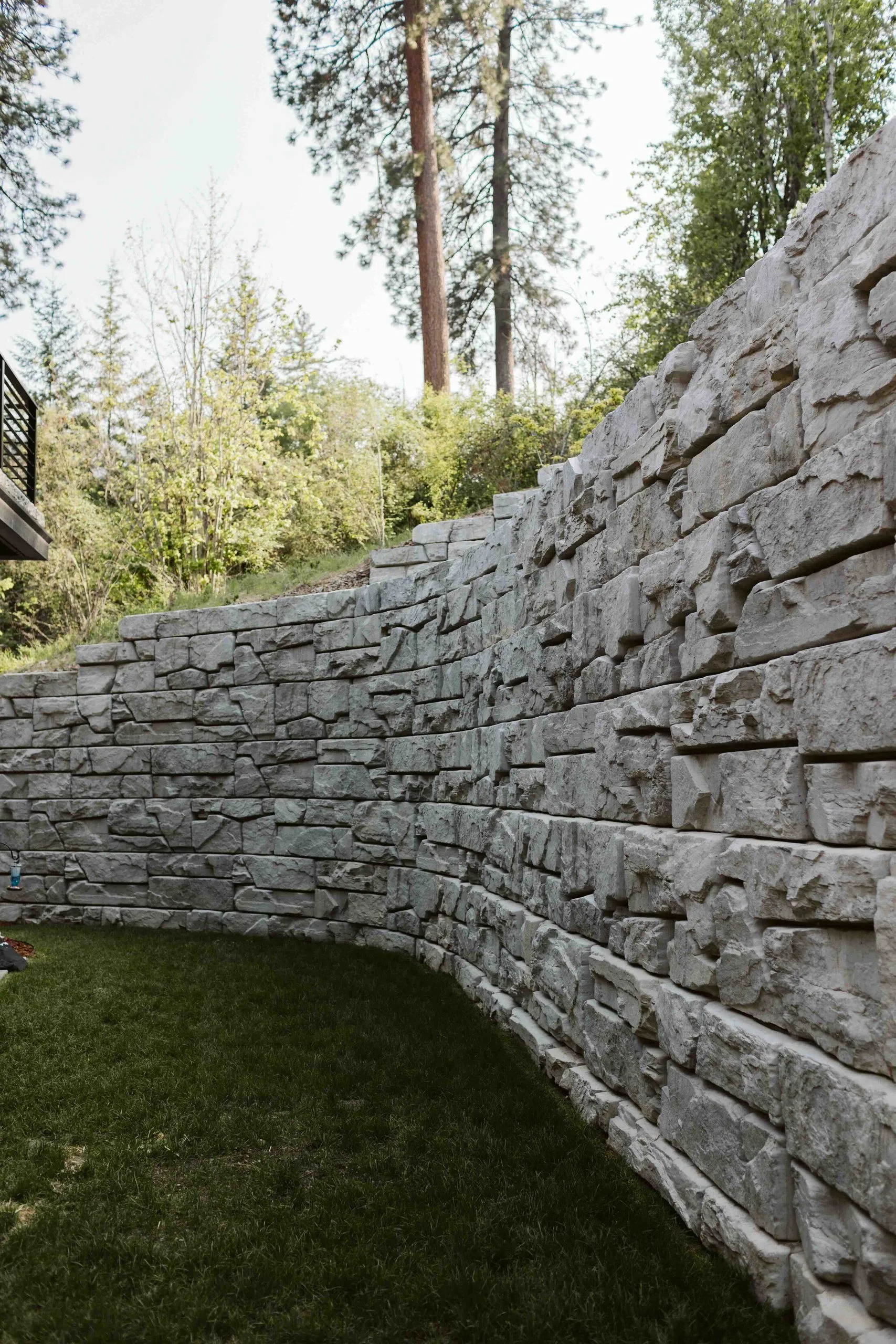 Tall curved block retaining wall holding back the hillside behind a narrow strip of lawn.