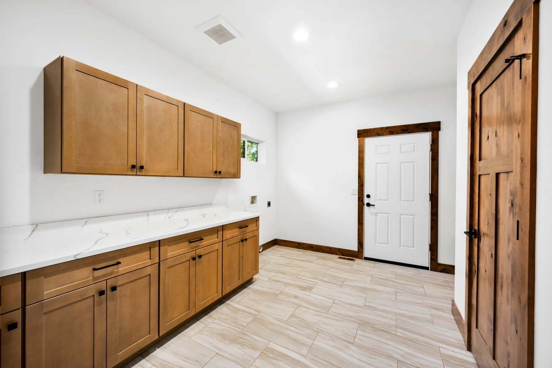 Laundry and mudroom with a long run of wood cabinets, a quartz counter and an exterior door.