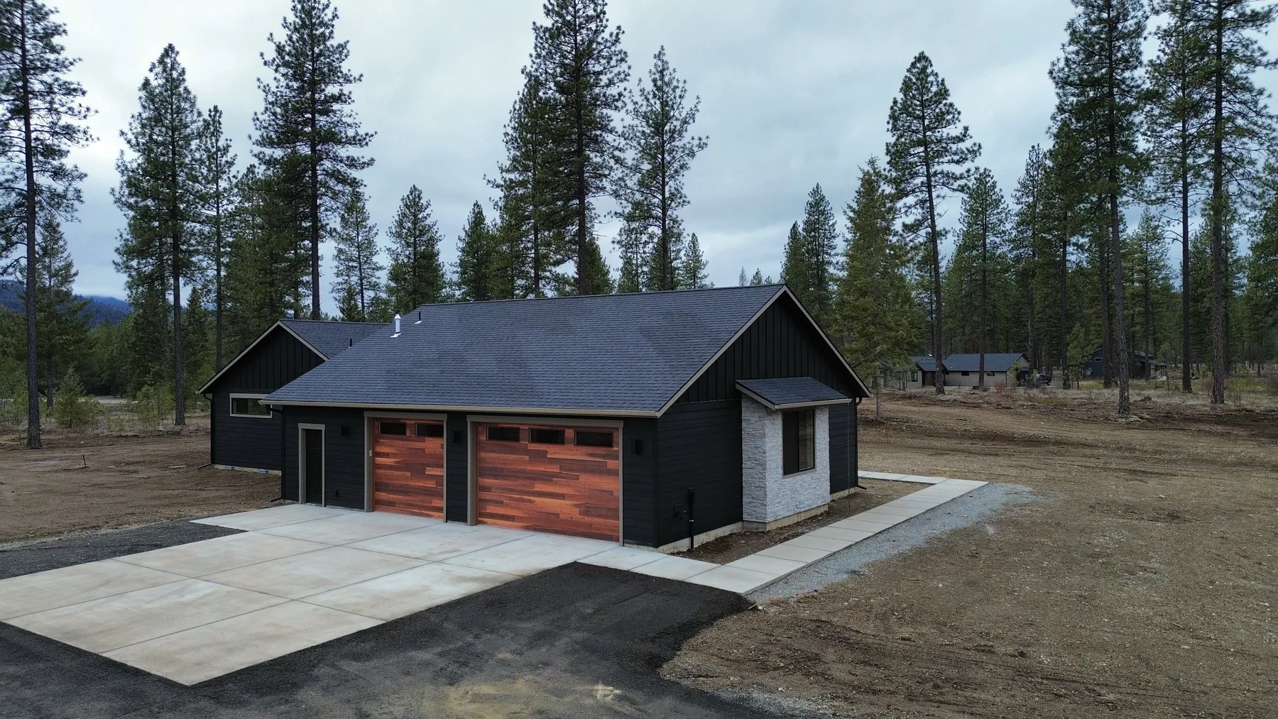 Garage side of The Summit with two cedar-toned garage doors, a new concrete apron and a paved drive.