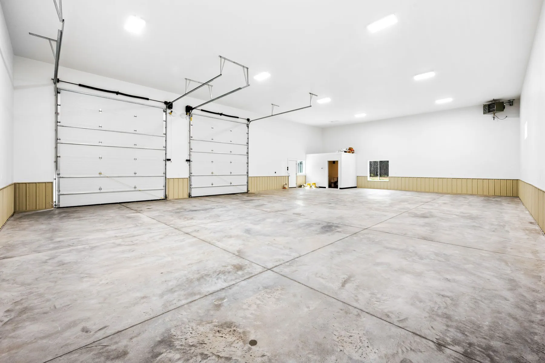 Inside the shop, an open bay with two overhead doors, a sealed concrete floor and bright lighting.