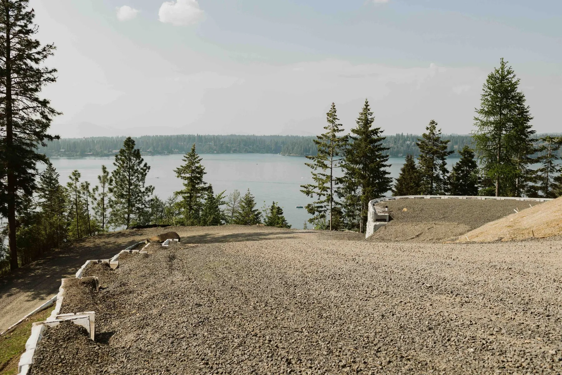 Leveled gravel pad at the top of the new driveway, with Hayden Lake and forested hills in the distance.