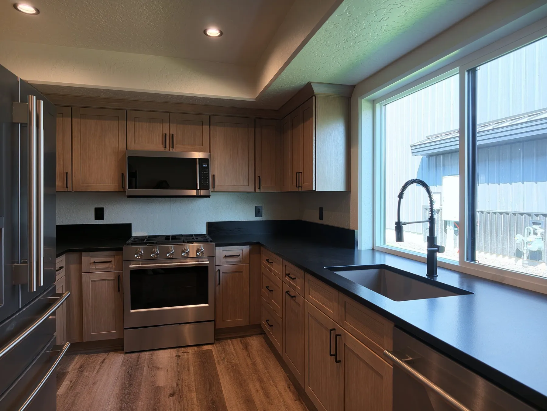 Full office kitchen with wood cabinets, black countertops, stainless appliances and a large window over the sink.