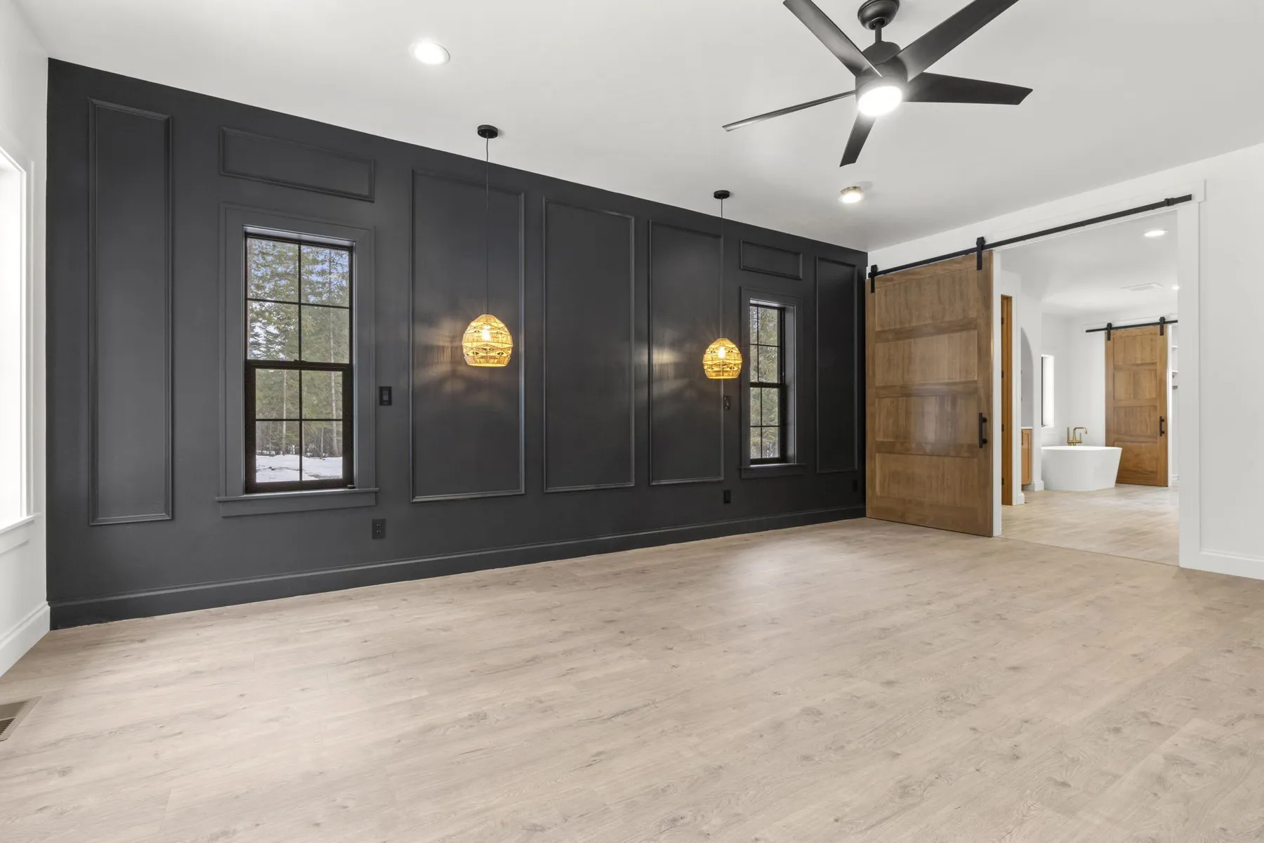 Primary suite with a black paneled accent wall, woven pendant lights and a sliding wood barn door to the bathroom.