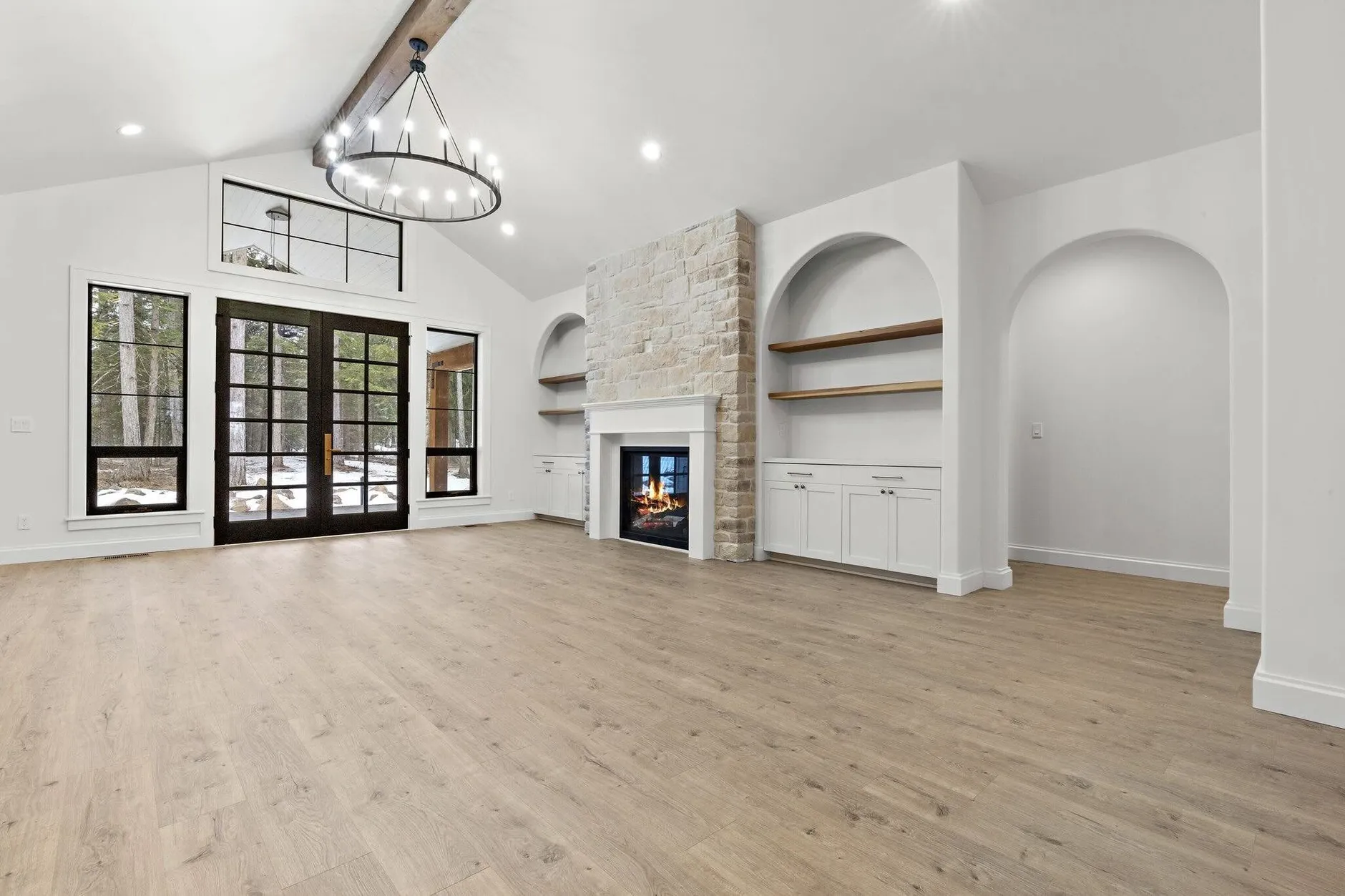 Vaulted great room at Rimrock Estate with a stone fireplace flanked by arched built-in shelves, black French doors and a wrought-iron chandelier.