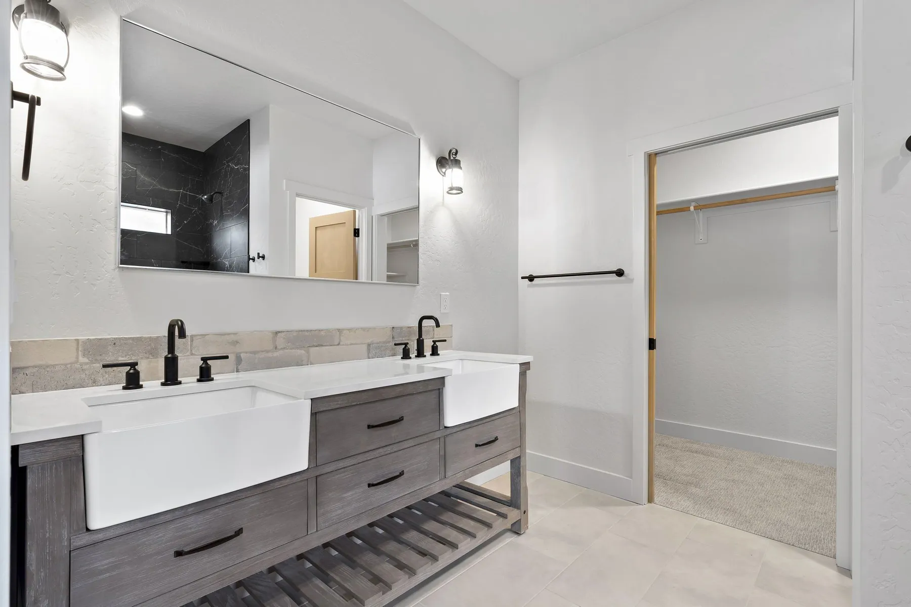 Primary bathroom with two farmhouse sinks on a weathered wood vanity, black fixtures and the walk-in closet through the doorway.