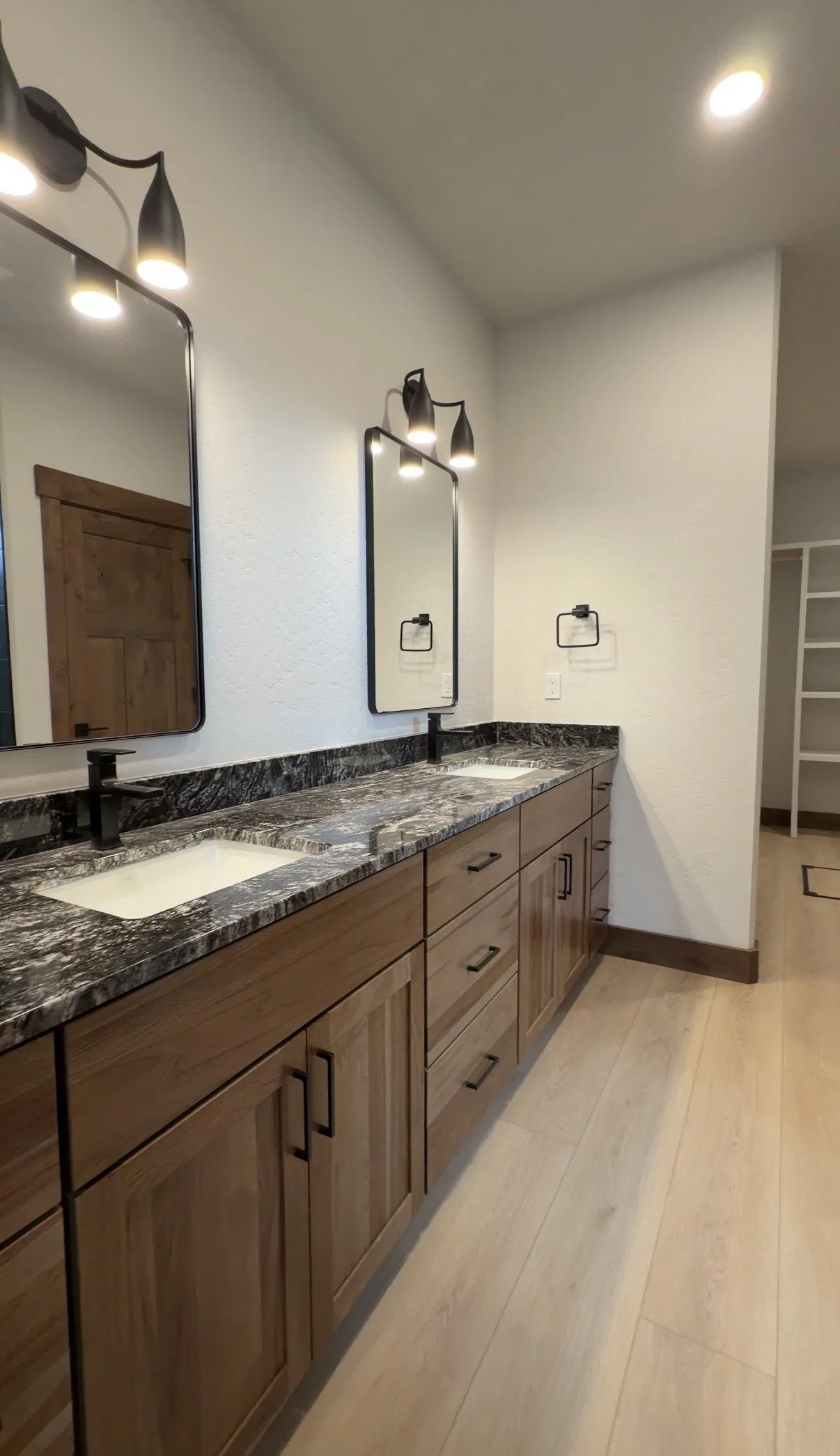 Bathroom with a long wood vanity, dark granite countertop, two sinks and black-framed mirrors.