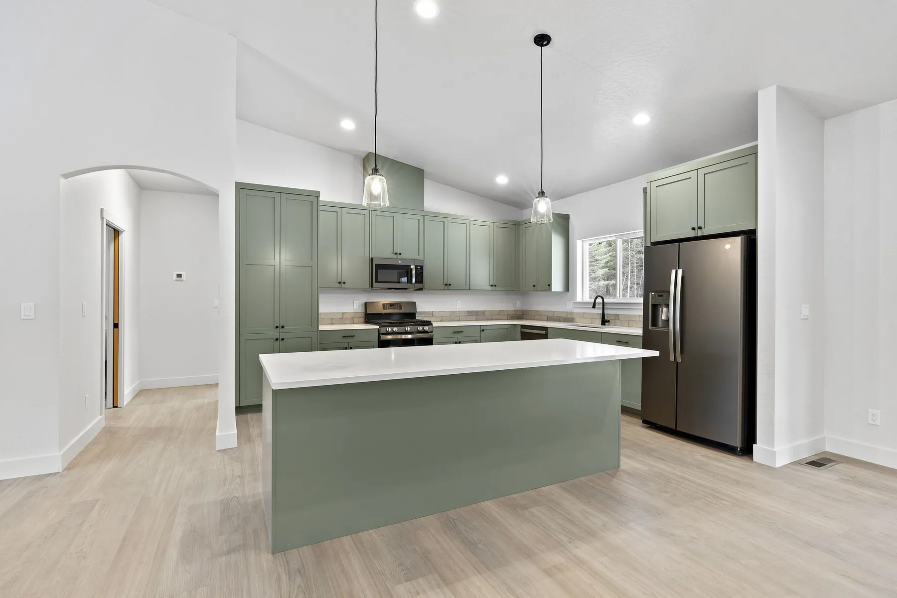 Kitchen with sage-green shaker cabinets, a green island with a white quartz top and black pendant lights.