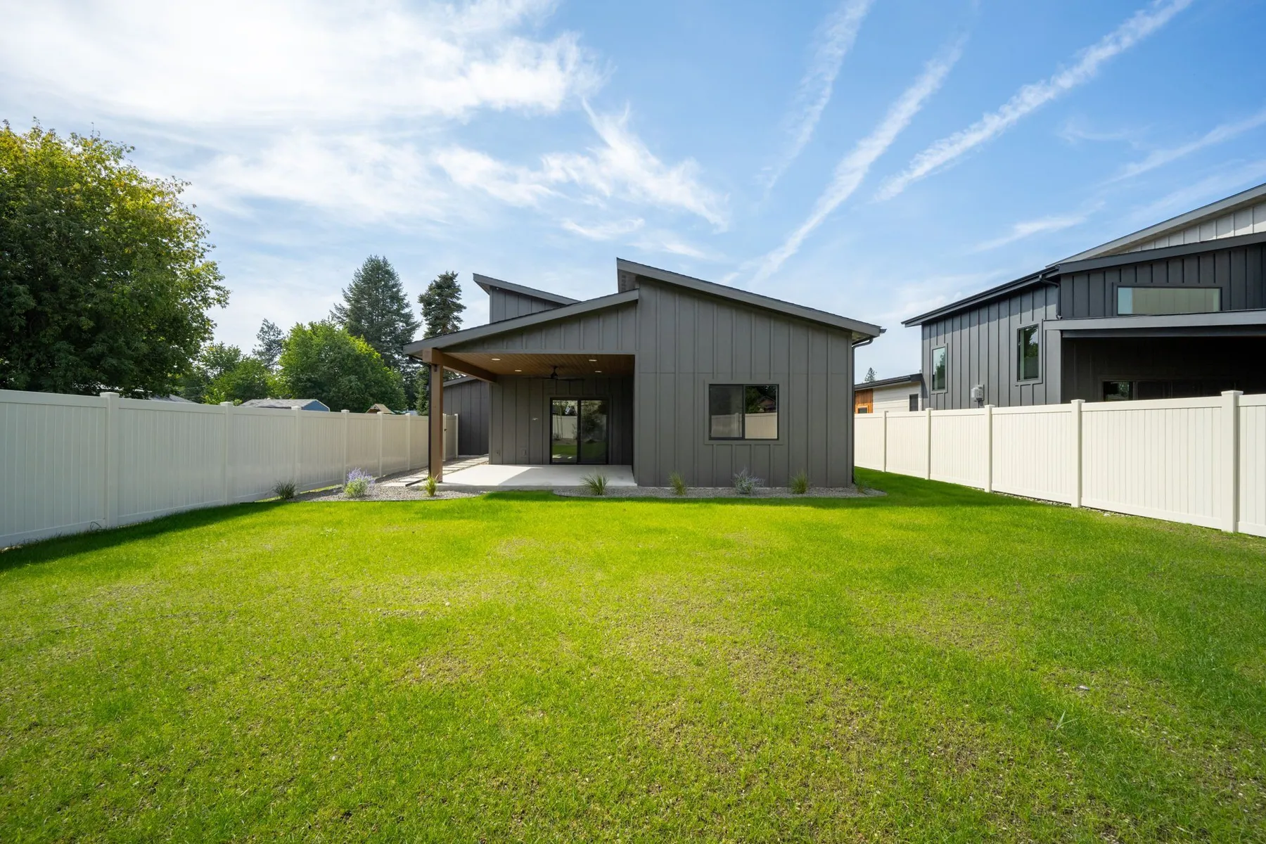 Backyard lawn behind the finished home, enclosed by a white vinyl privacy fence under a blue sky.
