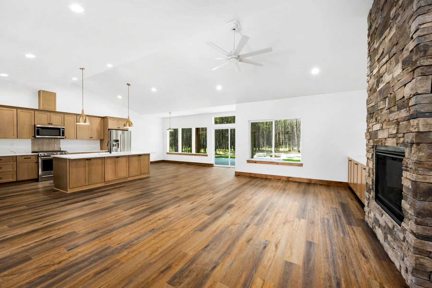 Open great room with wood-look plank flooring, a stacked-stone fireplace and an open kitchen with a long island.