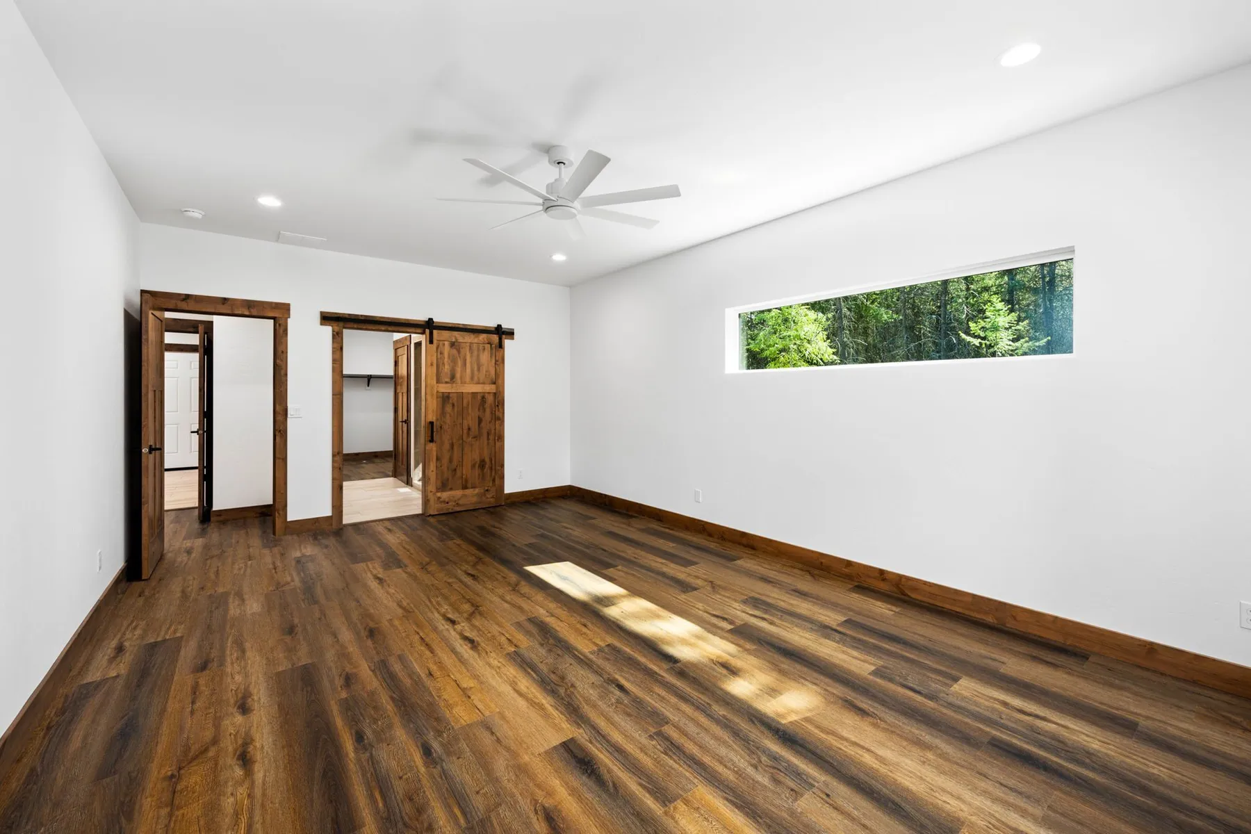 Primary bedroom with a long clerestory window, a ceiling fan and a sliding barn door to the bath.