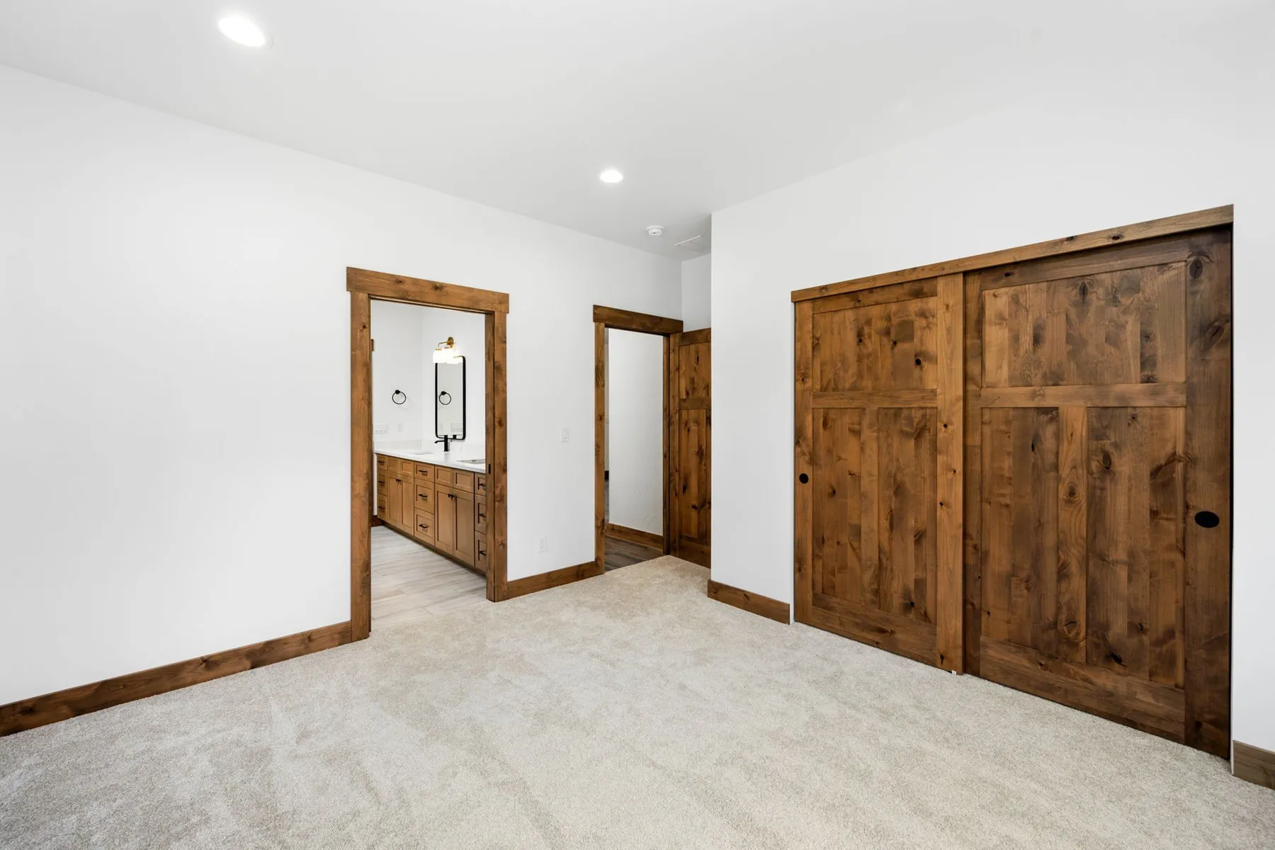 Carpeted bedroom with rustic knotty alder sliding closet doors and a doorway to the bathroom.