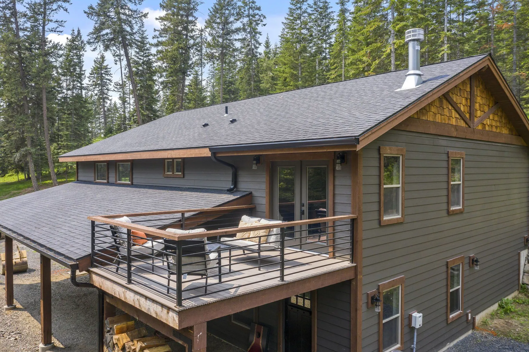 Rear of the shop home with a private upper deck with black railings, gray lap siding and a cedar-shingle gable.