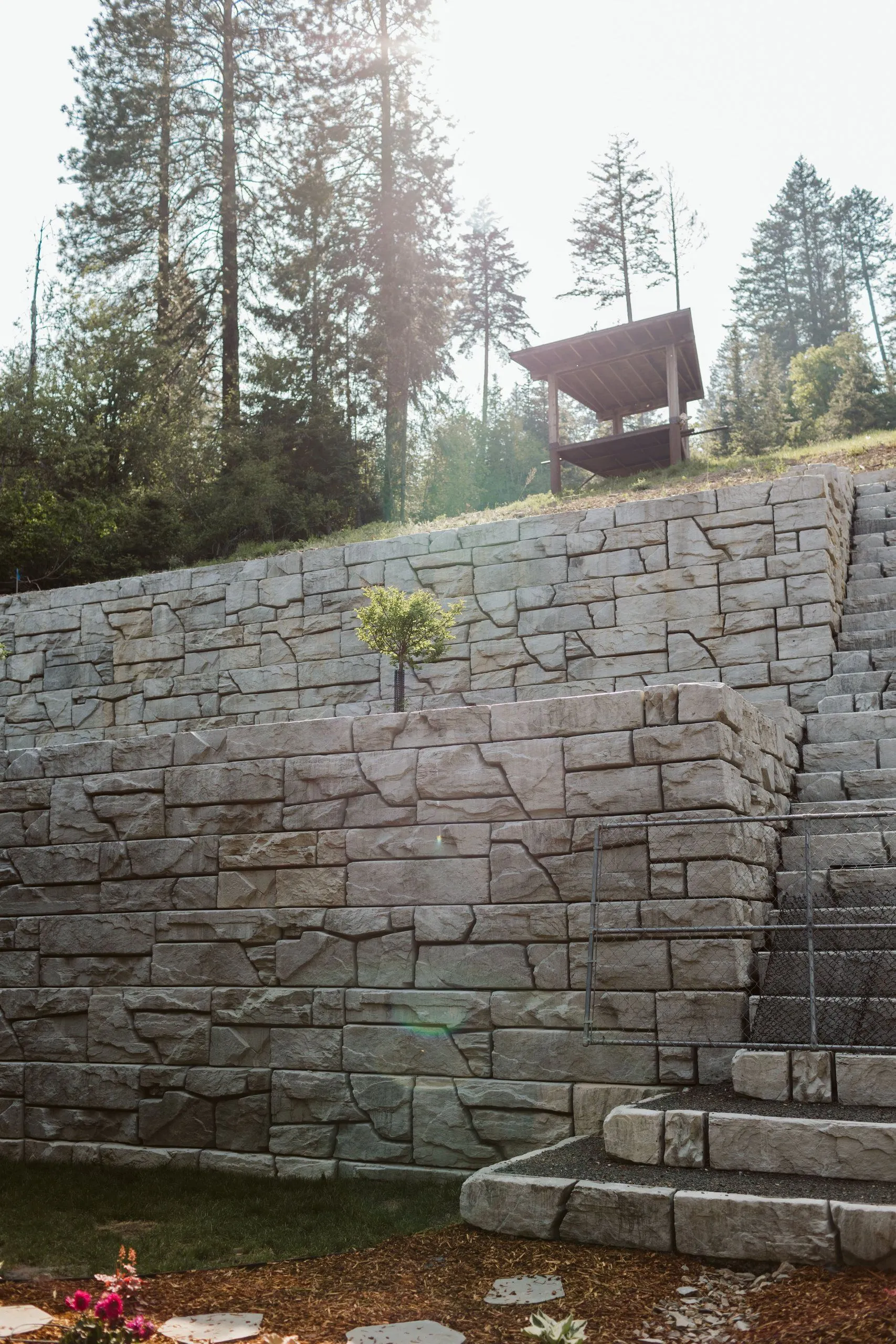 Stacked retaining walls and block stairs rising to a timber gazebo at the top of the slope.