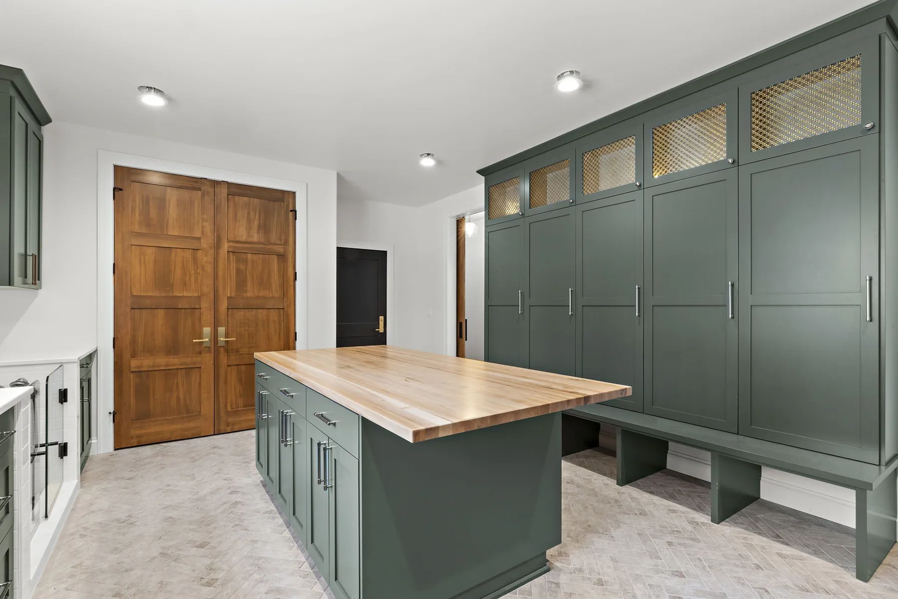 Mudroom with green built-in lockers, a butcher-block island and double wood doors.