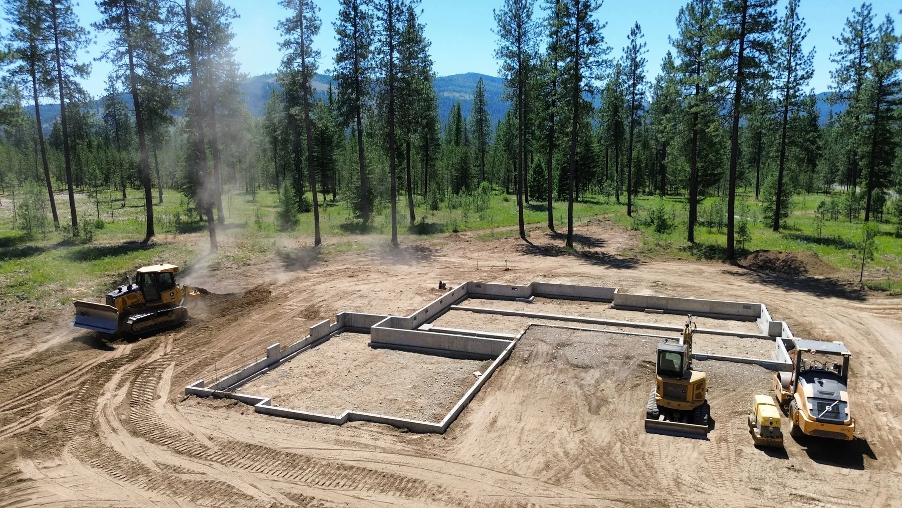 Dozer, excavator and compactor working around The Summit's new foundation on a cleared lot in the forest.