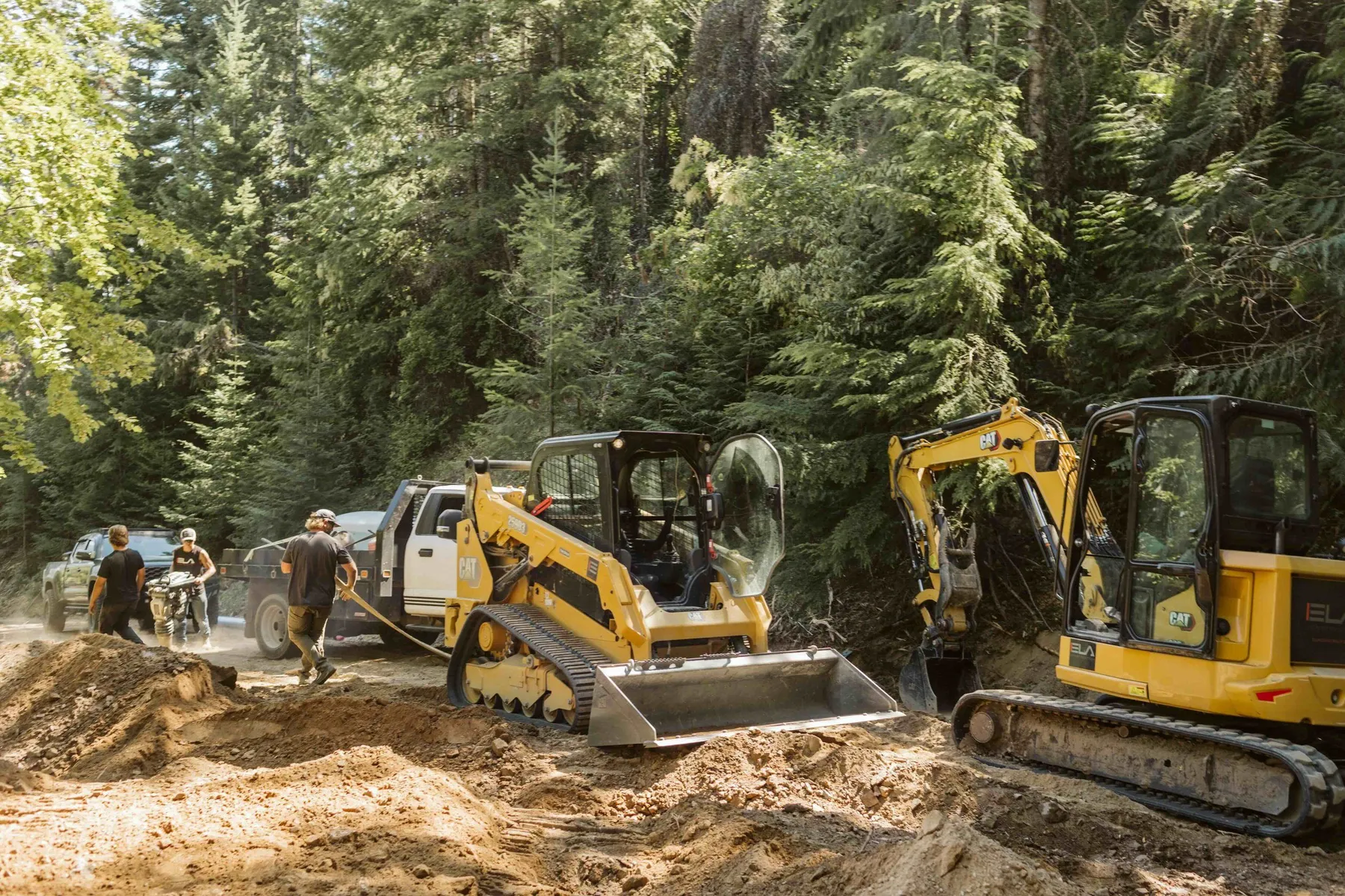 Crew with a skid steer and mini excavator preparing the driveway base among the trees.