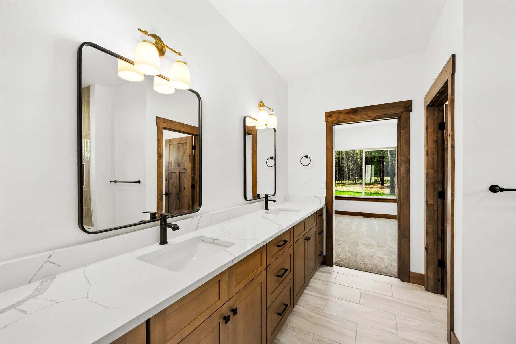 Primary bathroom with a long wood vanity, quartz countertop, black-framed mirrors and brass light fixtures.