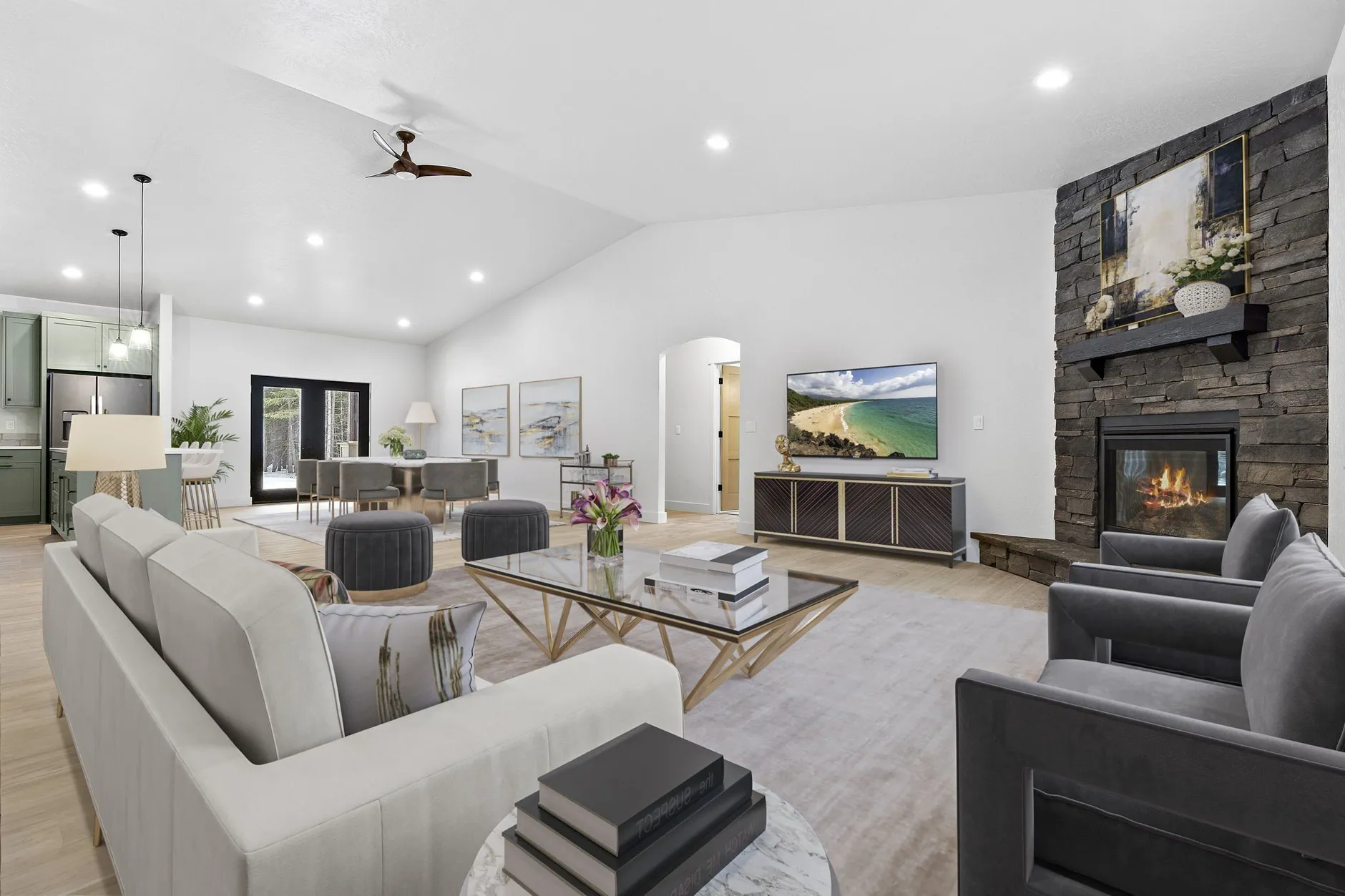 Vaulted living room with a dark stacked-stone fireplace, staged with a sectional and lounge chairs, open to a sage-green kitchen and dining area.