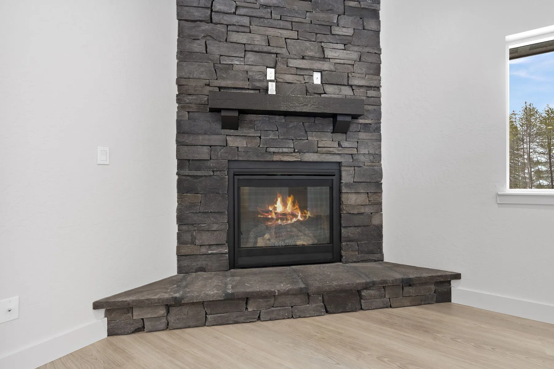 Close-up of the floor-to-ceiling stacked-stone fireplace with a raised stone hearth and a lit gas fire.