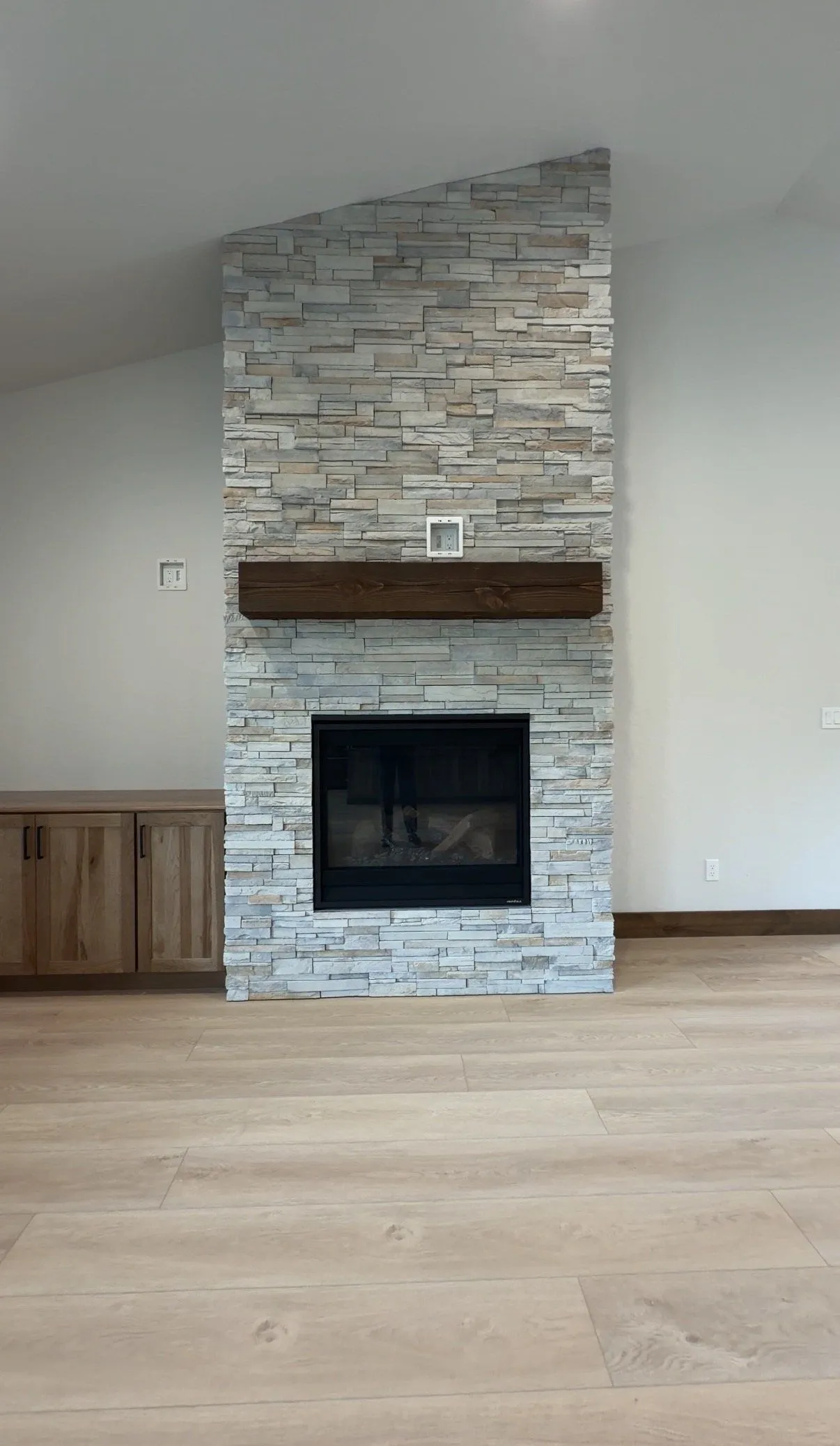 Floor-to-ceiling stacked-stone fireplace with a rustic wood mantel beside built-in wood cabinets.