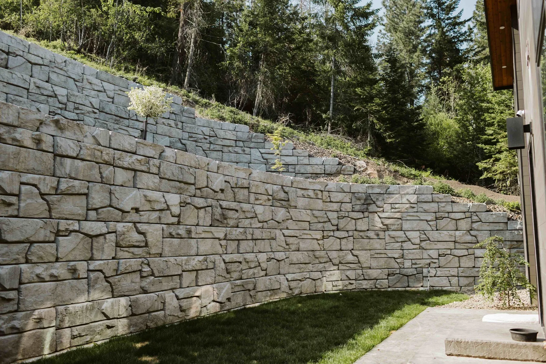 Two tiers of stone-textured block retaining wall curving along a new lawn beside the house.