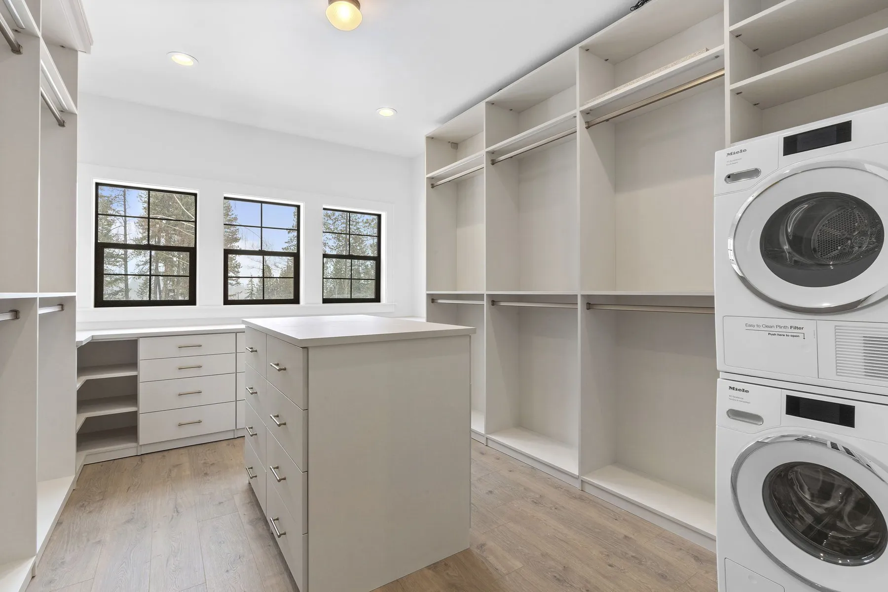 Custom primary walk-in closet with an island, open shelving and a stacked washer and dryer.