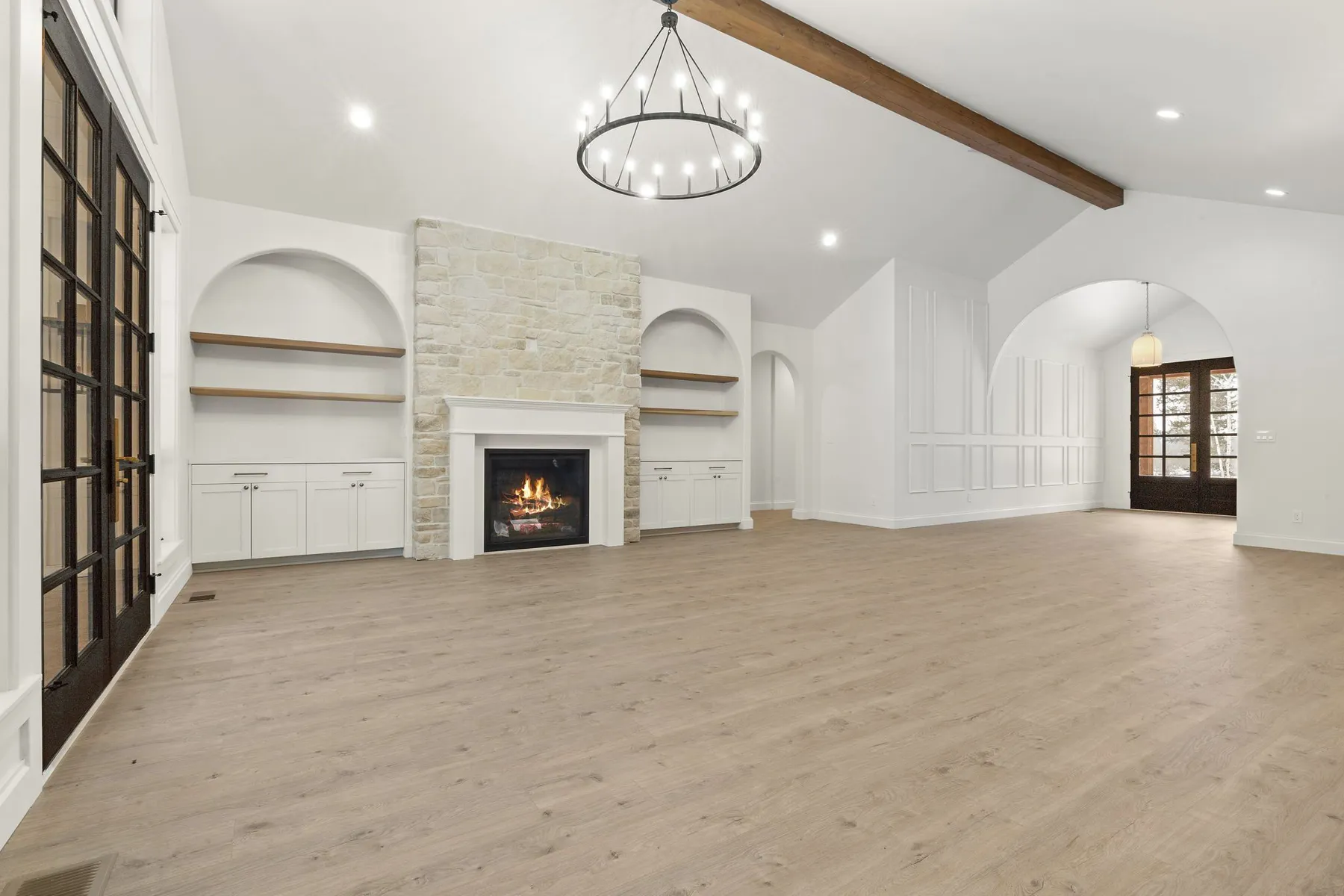 Great room with twin arches framing a stone-surround fireplace, built-in shelving and a ring chandelier under the vaulted ceiling.