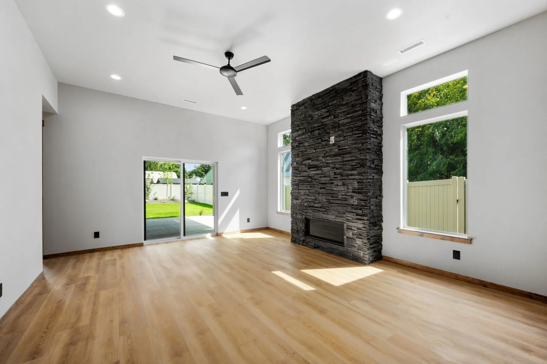Living room with a floor-to-ceiling black stacked-stone fireplace, light plank flooring and a sliding door to the backyard.