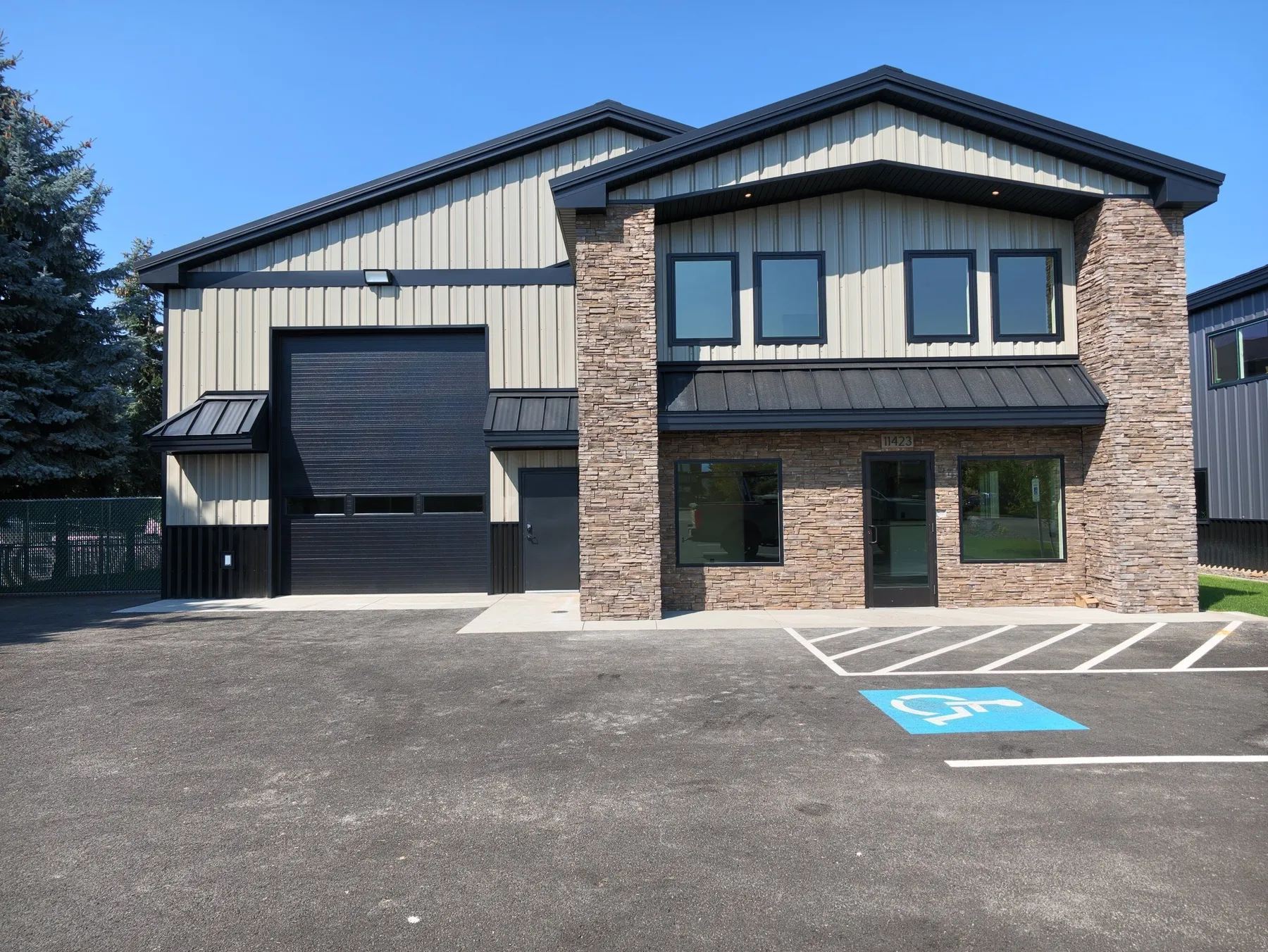Front of the facility with a stacked-stone office entry, black-framed windows, a metal awning and a large roll-up warehouse door.