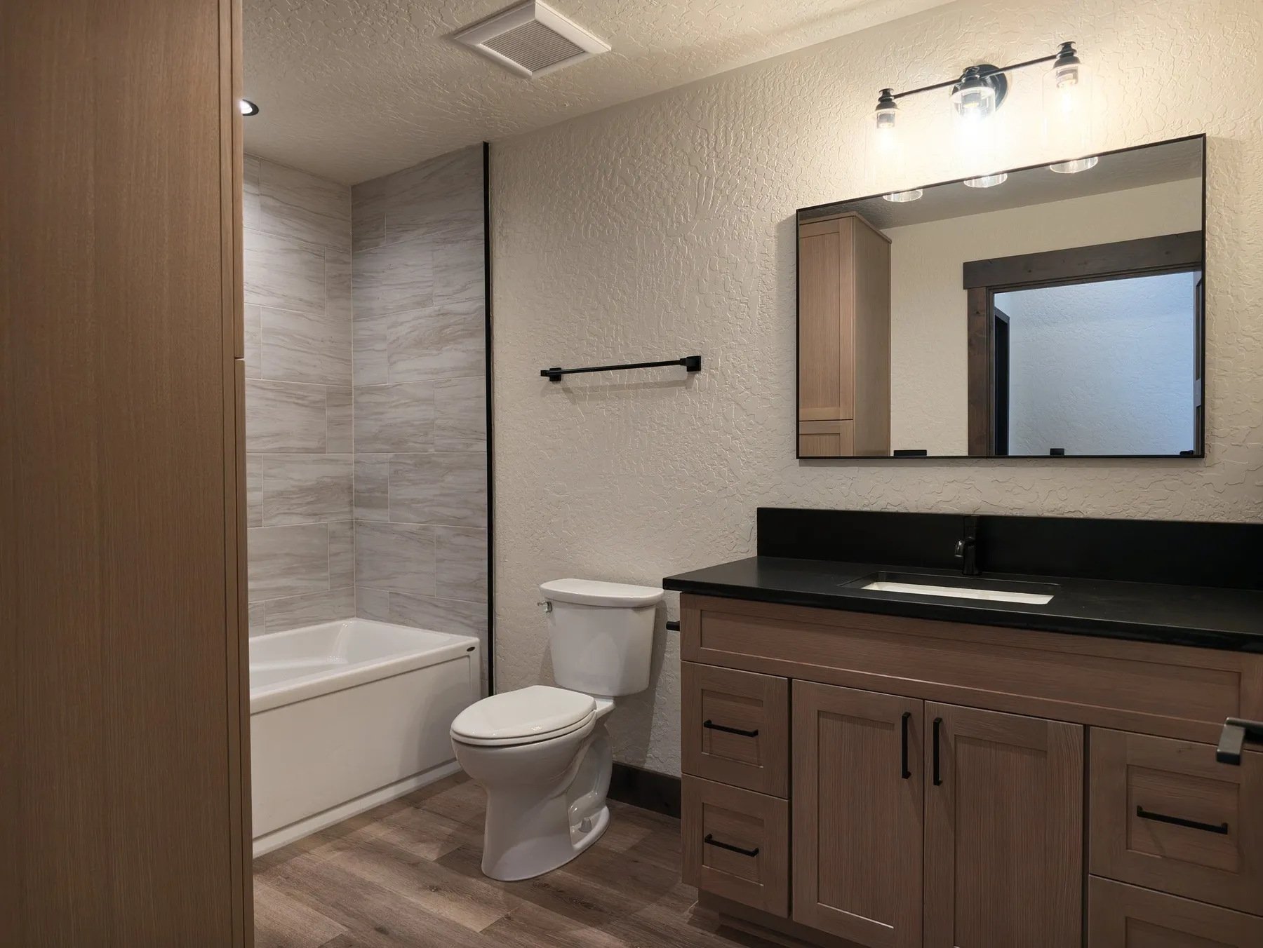 Upstairs full bathroom with a tub and tile surround, a wood vanity with black countertop and a black-framed mirror.