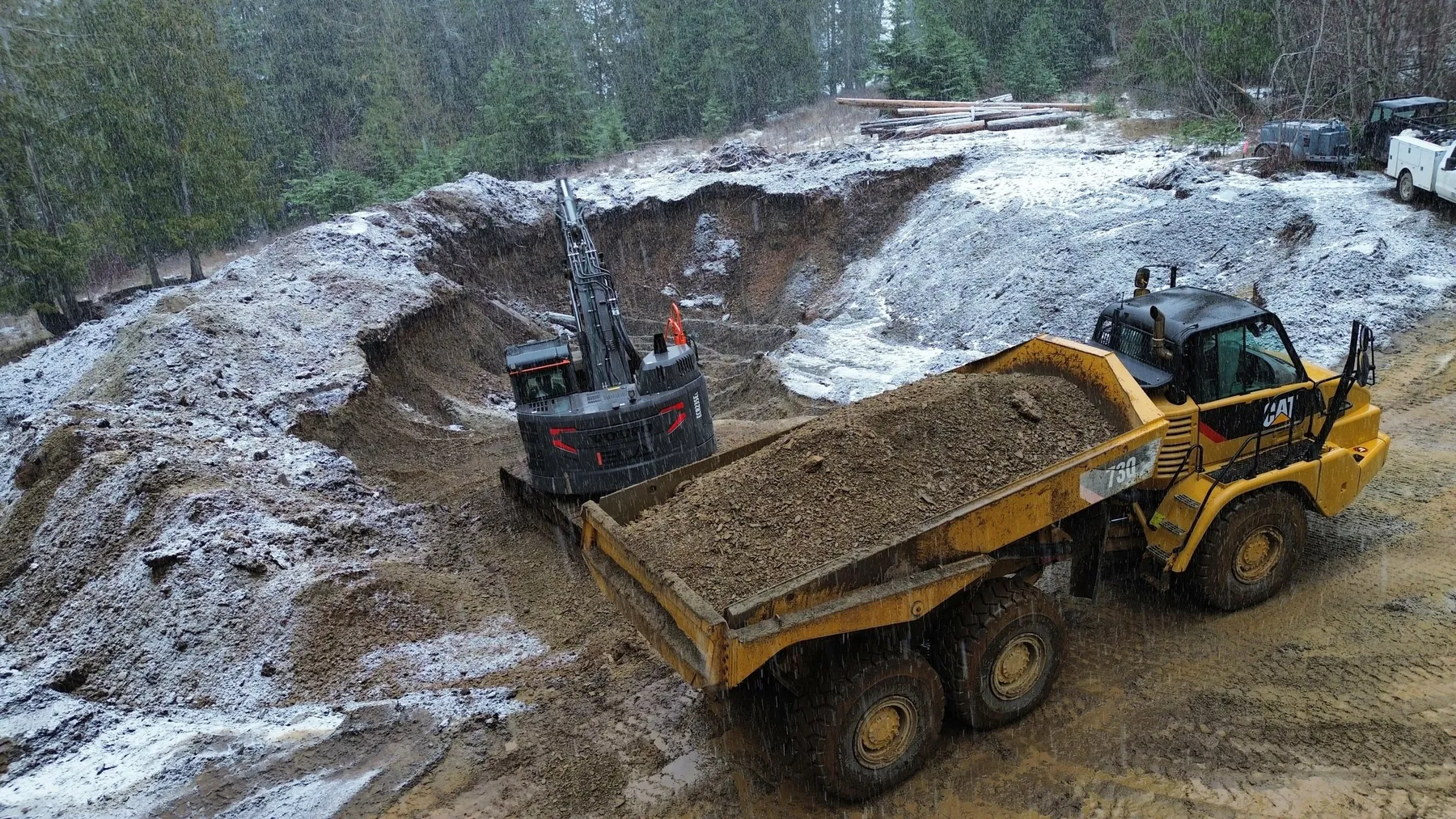 Excavator loading dirt into a yellow CAT articulated dump truck in a large frosty cut on the hillside.