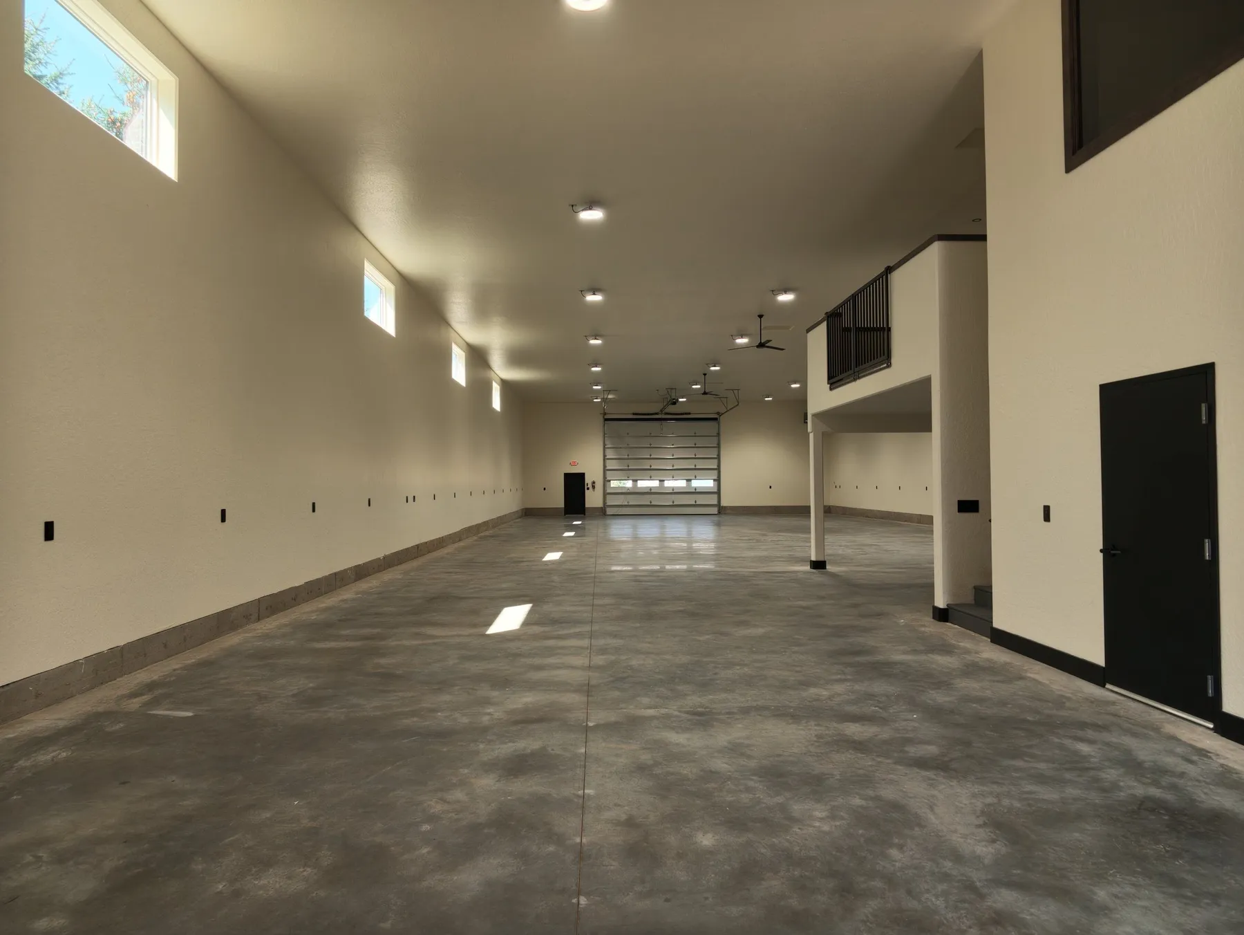 Long warehouse bay with a polished concrete floor, high clerestory windows and an overhead door at the far end.