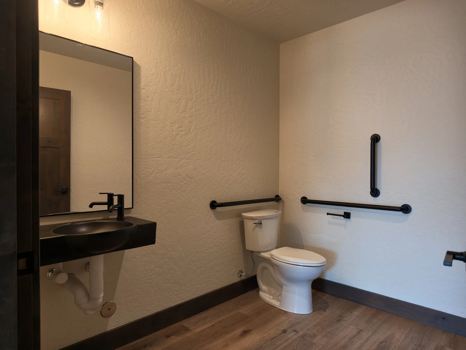 ADA-accessible half bath with a wall-mounted black sink, grab bars beside the toilet and wood-look flooring.