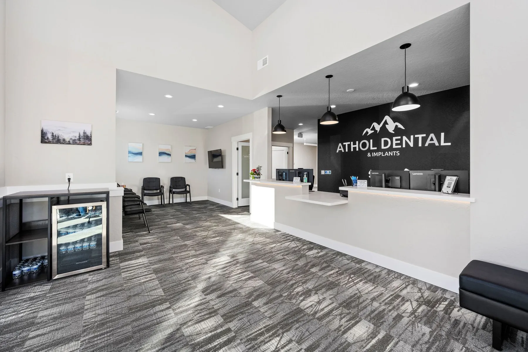 Athol Dental reception desk with a black logo wall, pendant lights and a waiting area with patterned gray carpet.