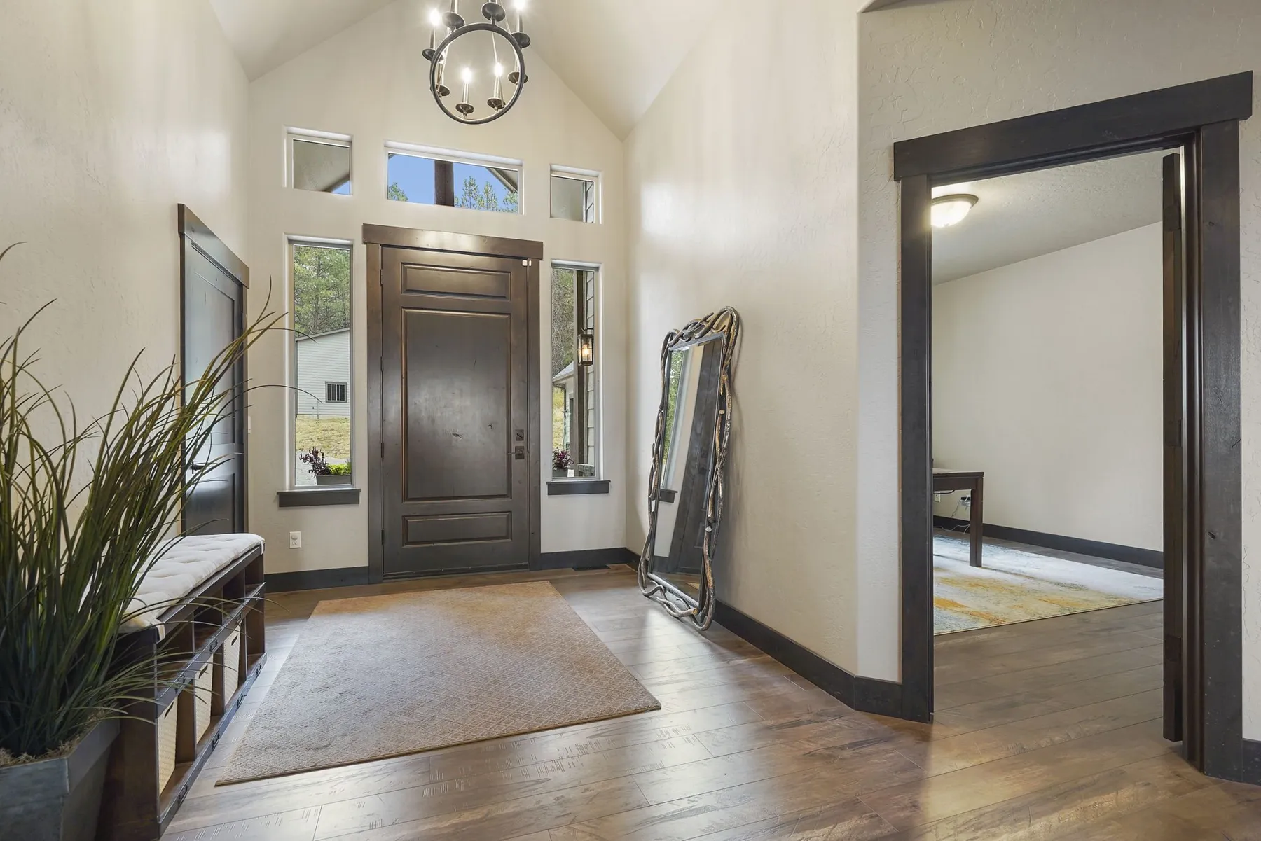 Vaulted entry with a dark wood front door, transom windows, a bench and a doorway into a side room.
