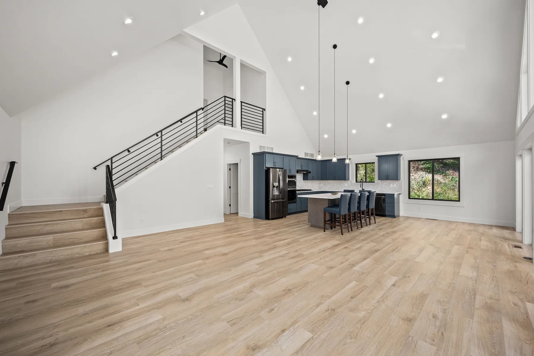Vaulted great room with a black metal stair railing up to the loft and an open kitchen with blue cabinets.