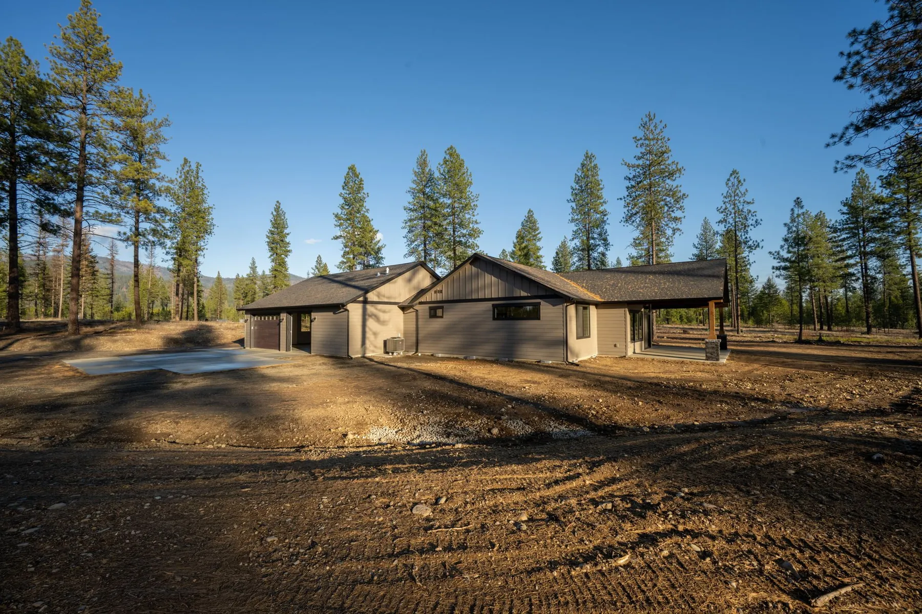 Side view of the Reverse Summit home and its attached garage, set back on a dirt lot surrounded by ponderosa pines.