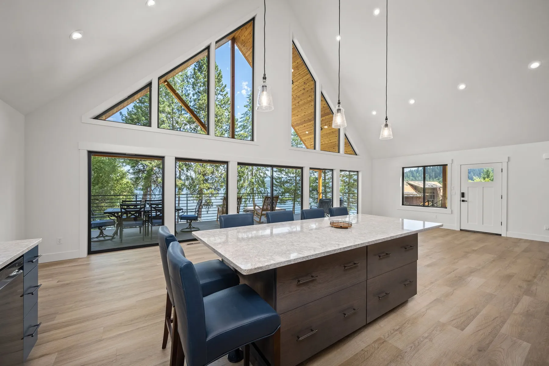 Kitchen island with a quartz top and blue bar stools beneath soaring triangular windows facing the lake.