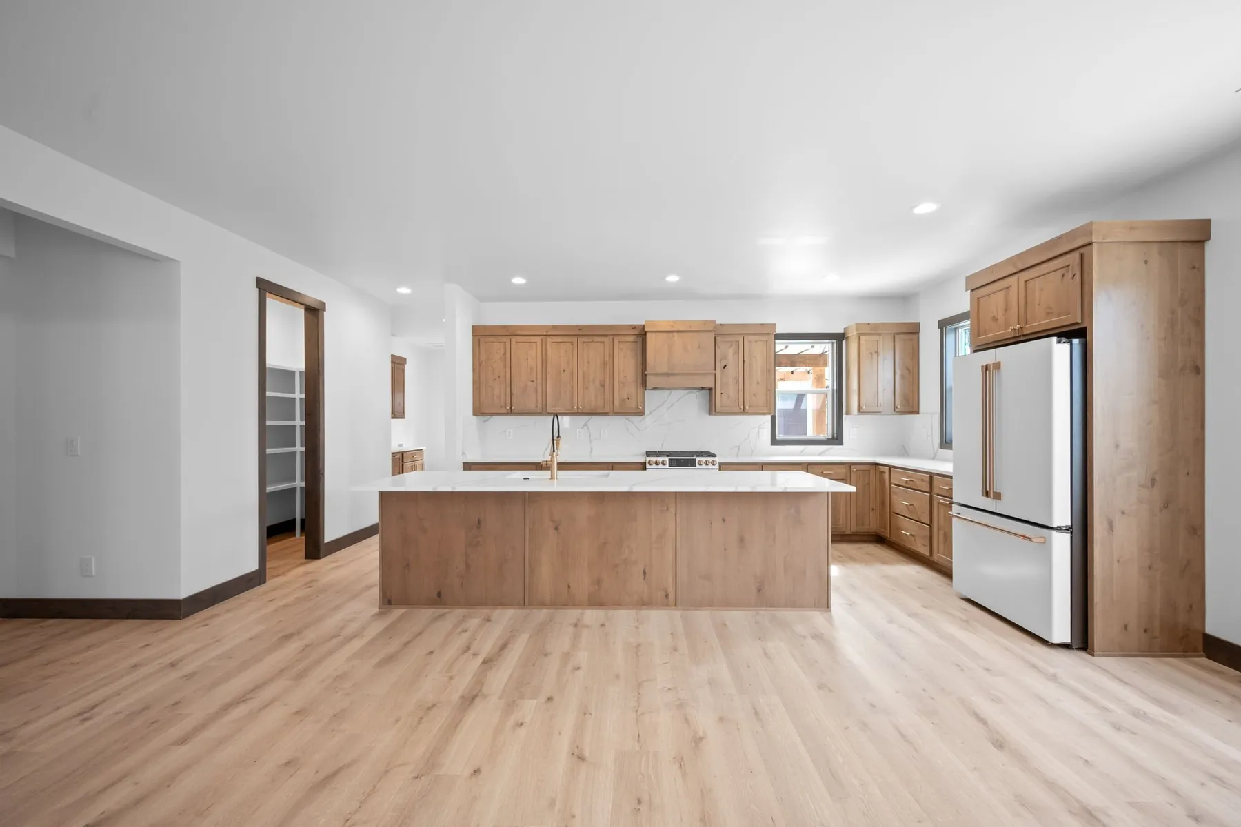 Kitchen with knotty alder cabinetry, a long quartz island, white appliances and light plank flooring.