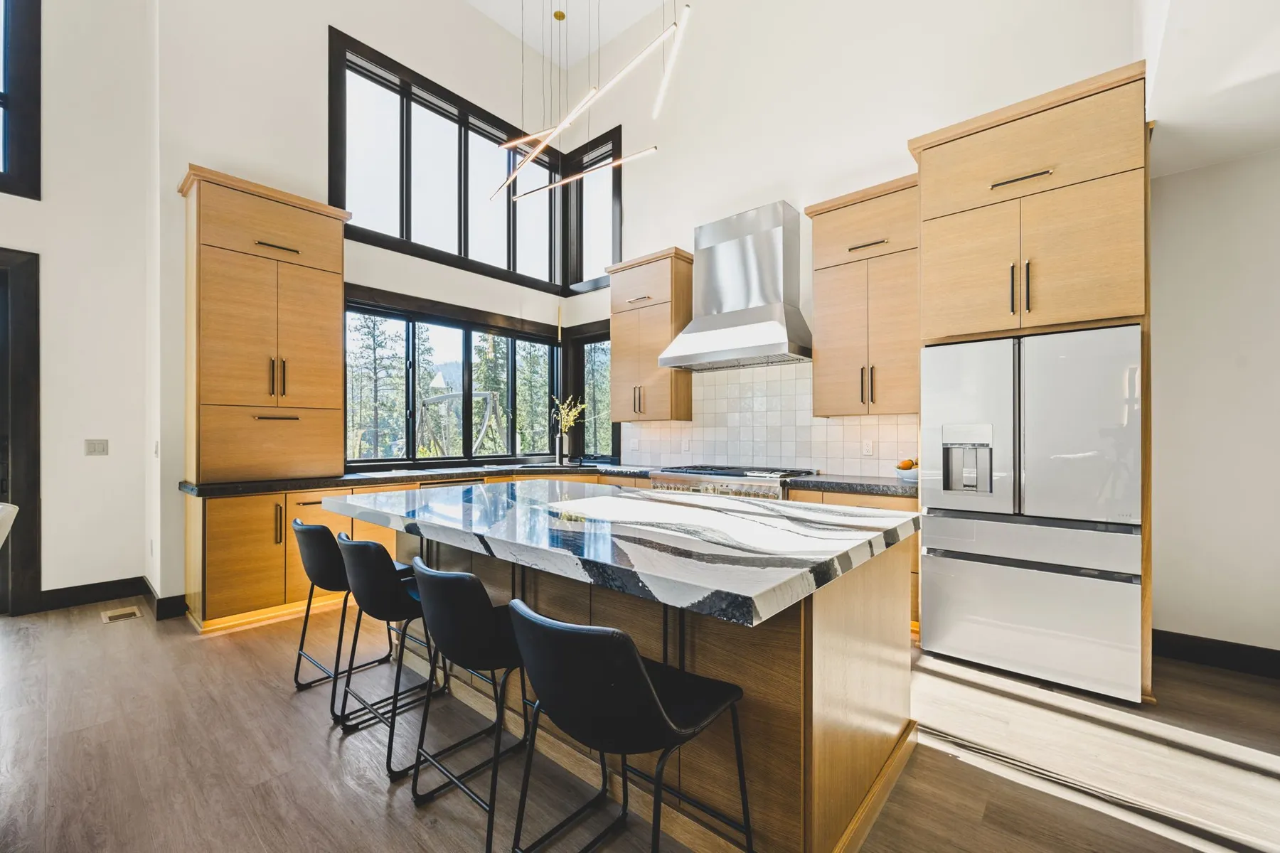 Kitchen with light wood cabinets, a marble waterfall island with black bar stools and clerestory windows above.