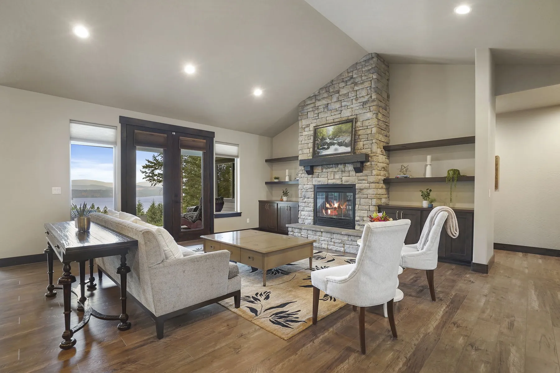 Living room with a stacked-stone fireplace, built-in shelves and French doors looking out toward Coeur d'Alene Lake.