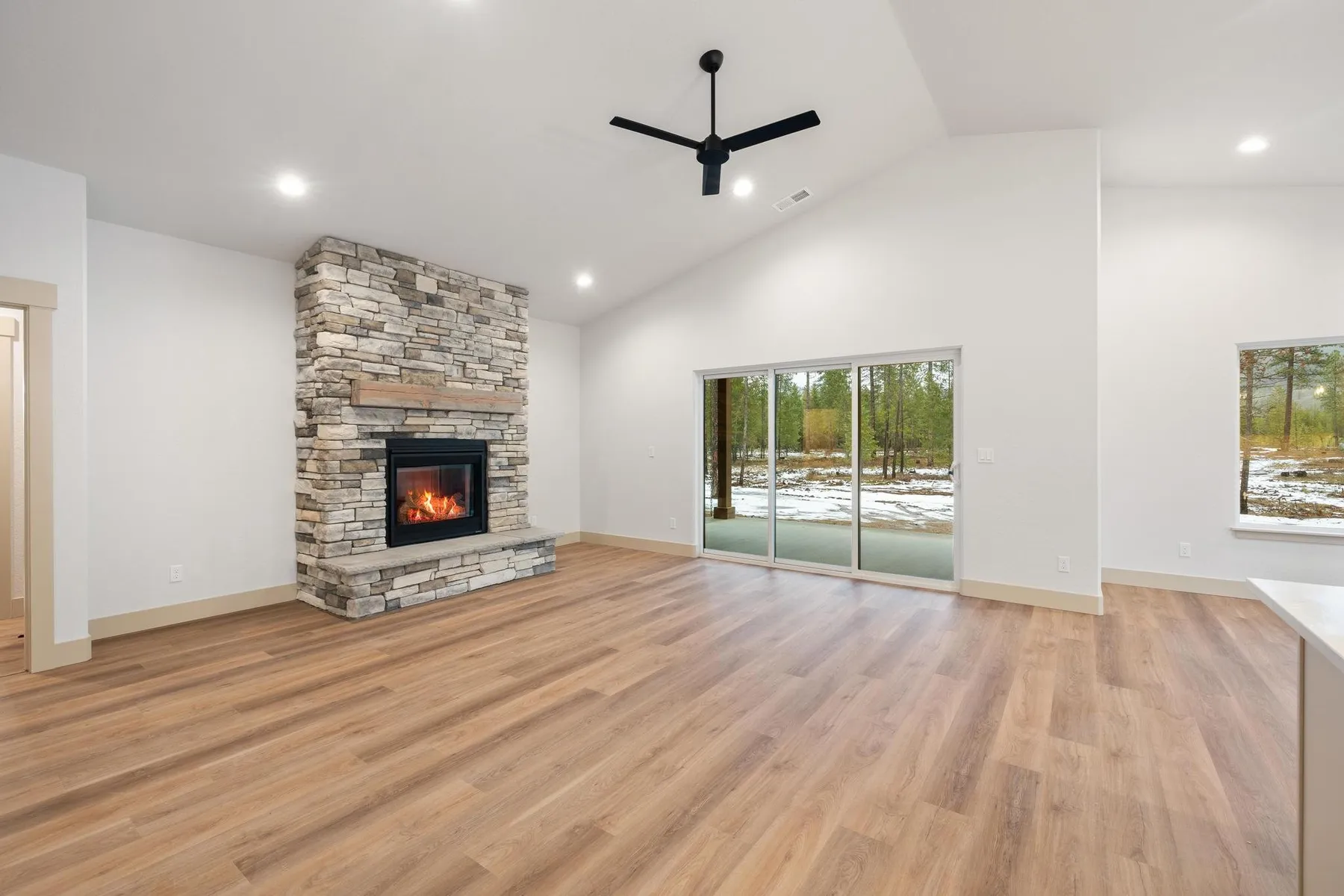 Vaulted living room with a stacked-stone fireplace and wood mantel, a ceiling fan and sliding doors to the back patio.