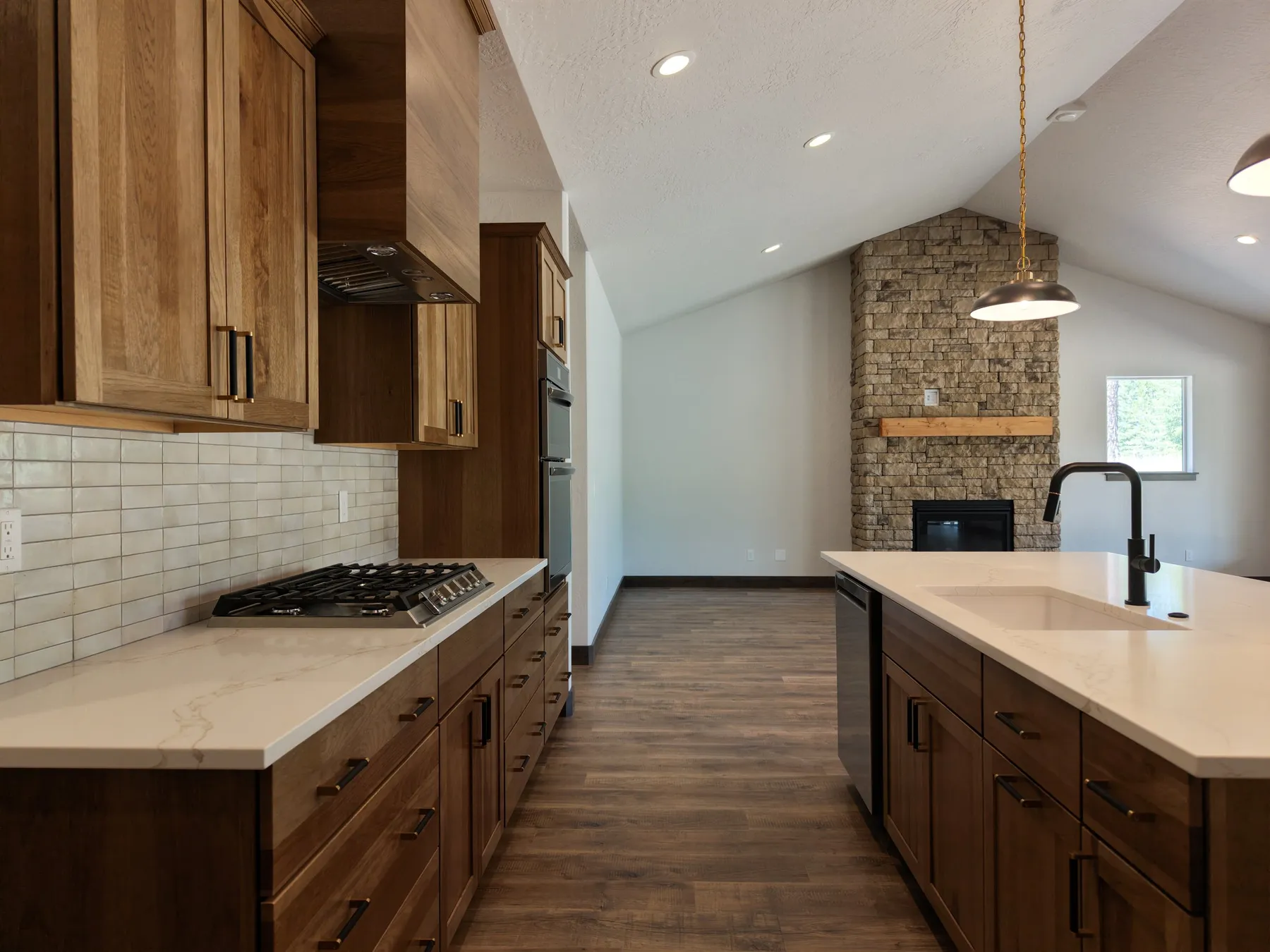 Kitchen counter with a gas cooktop and hickory cabinets, looking toward a stone-surround fireplace in the vaulted living room.
